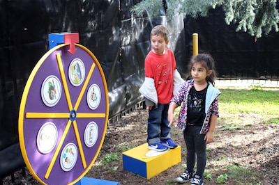 Two young children play with an interactive playground outside.