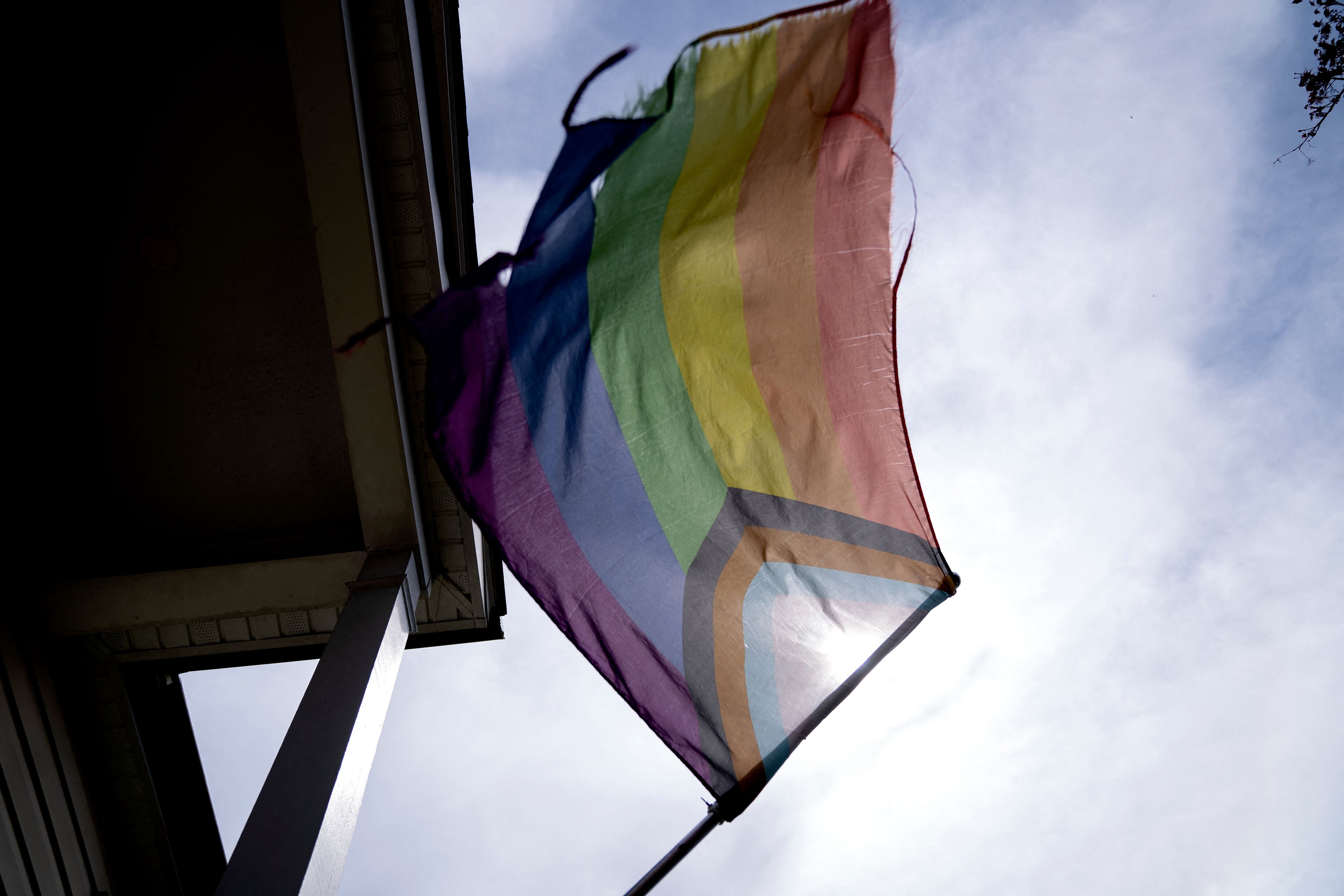 A slightly tattered Pride flag waves from a standard on a front porch.
