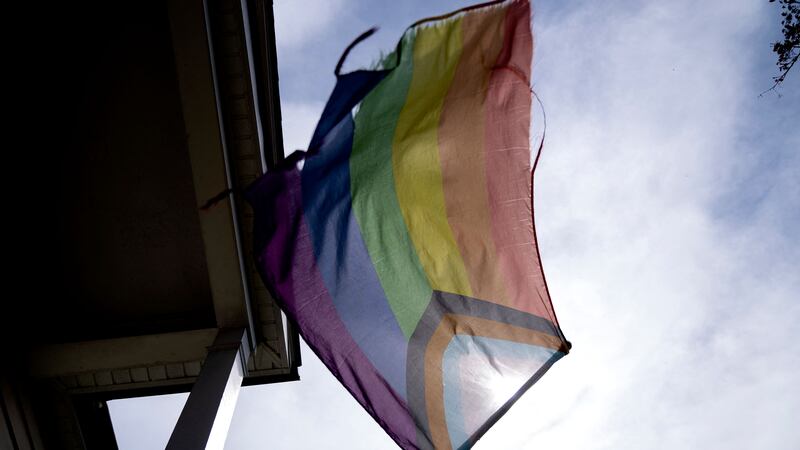 A slightly tattered Pride flag waves from a standard on a front porch.