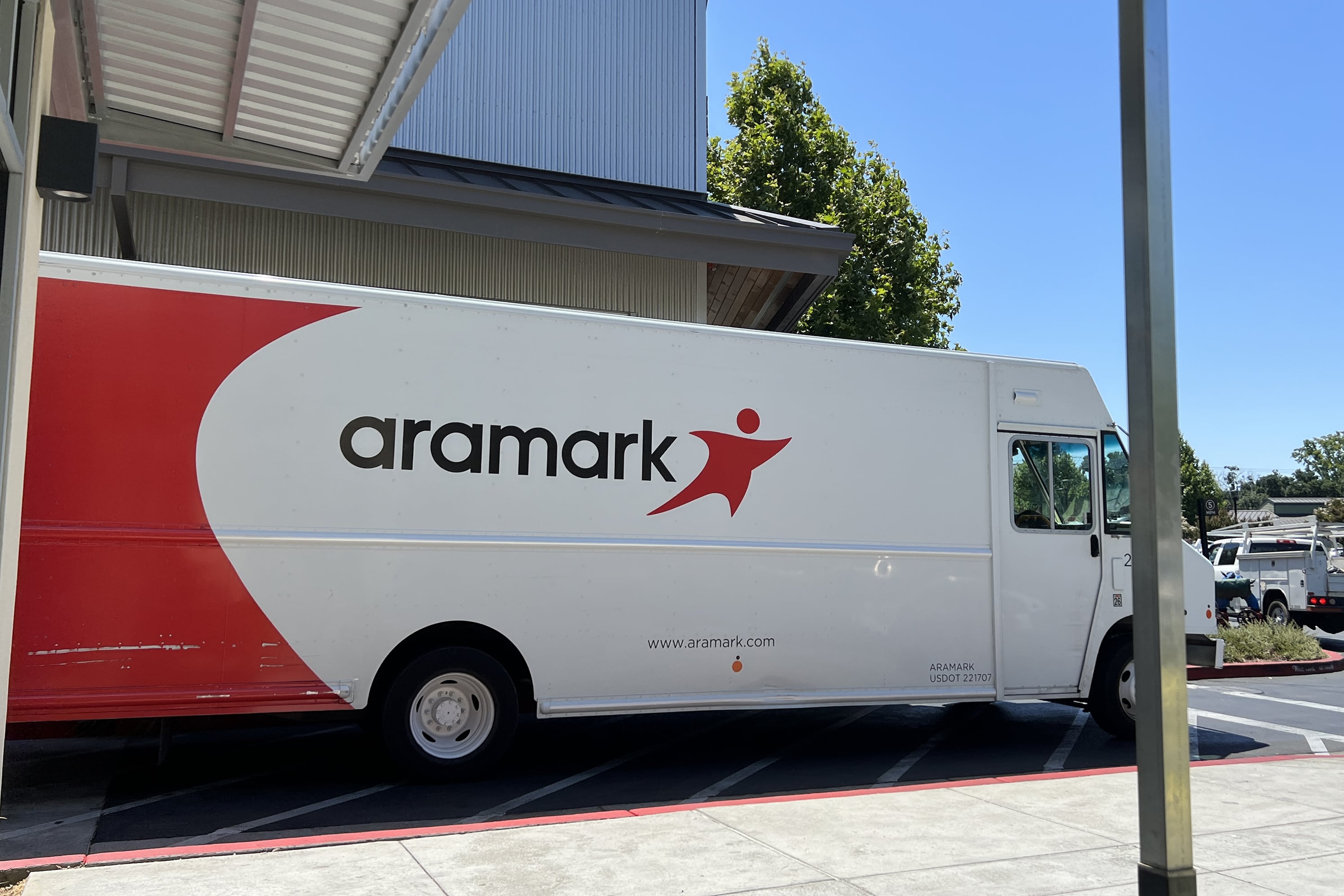 A white and red large delivery truck is parked outside with the word "Aramark" on the side with blue sky in the background.