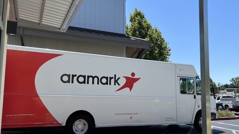 A white and red large delivery truck is parked outside with the word "Aramark" on the side with blue sky in the background.