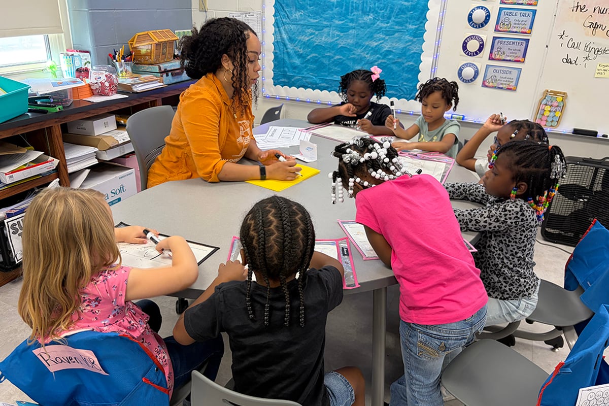 A woman in an orange top sits at a table with small children.