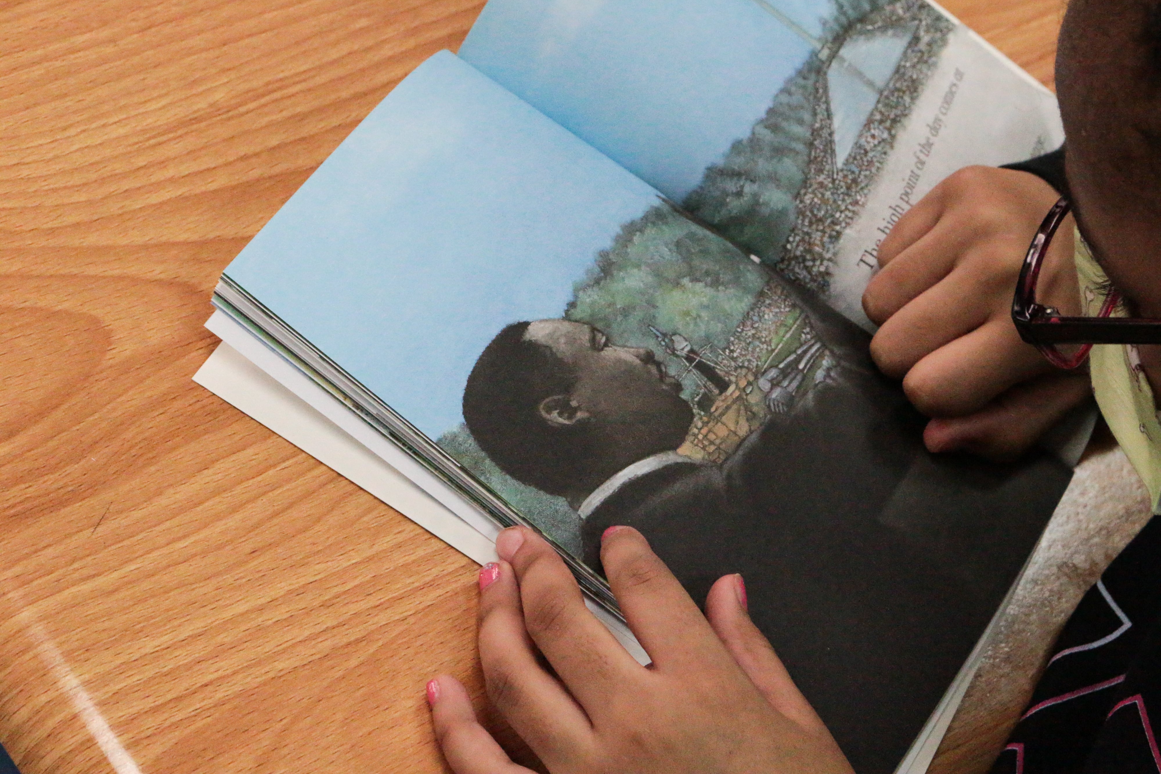 A young student reads a book depicting a drawing of Dr. Martin Luther King Jr. at their desk.