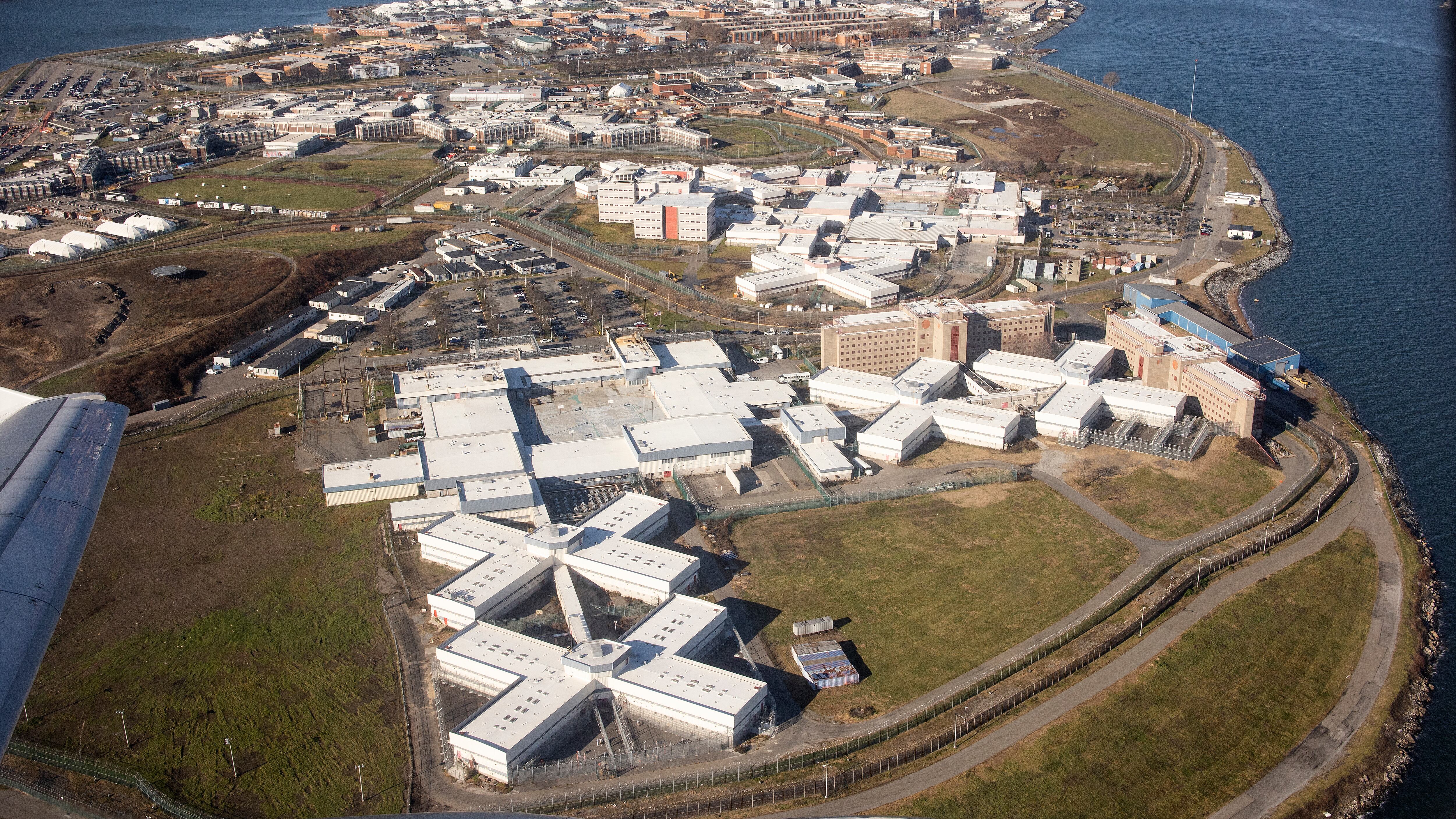 An arial view of Rikers Island with its dozens of white buildings scattered on the land.