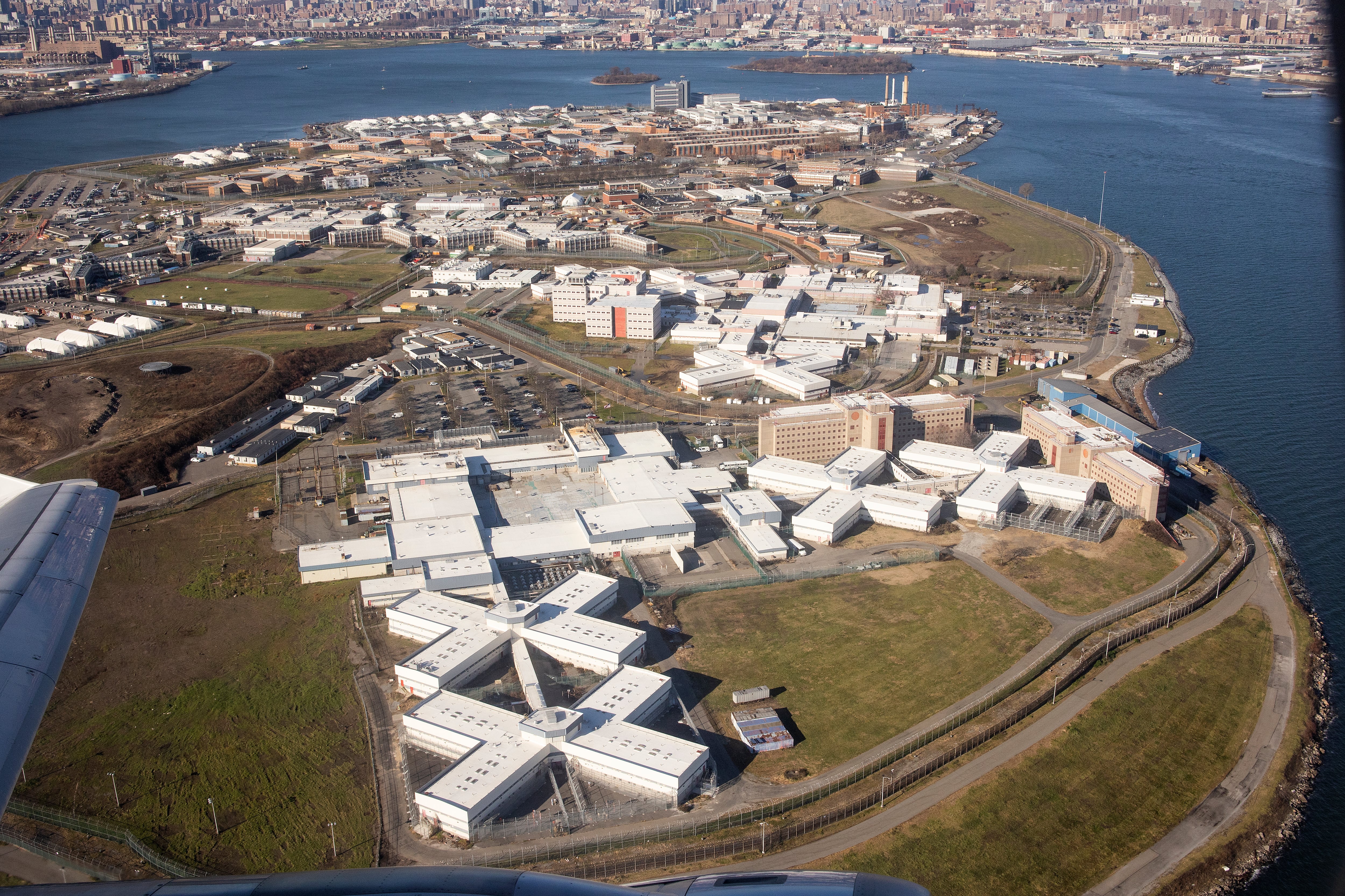 An arial view of Rikers Island with its dozens of white buildings scattered on the land.