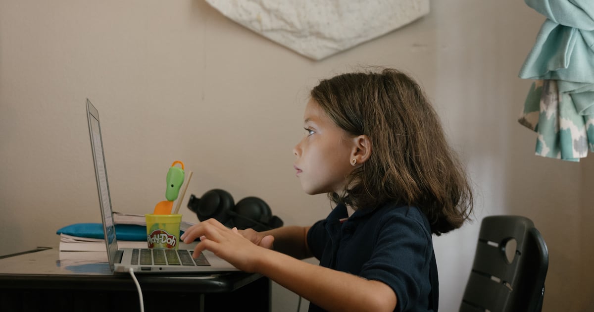 A young girl sits at a desk working on a computer.