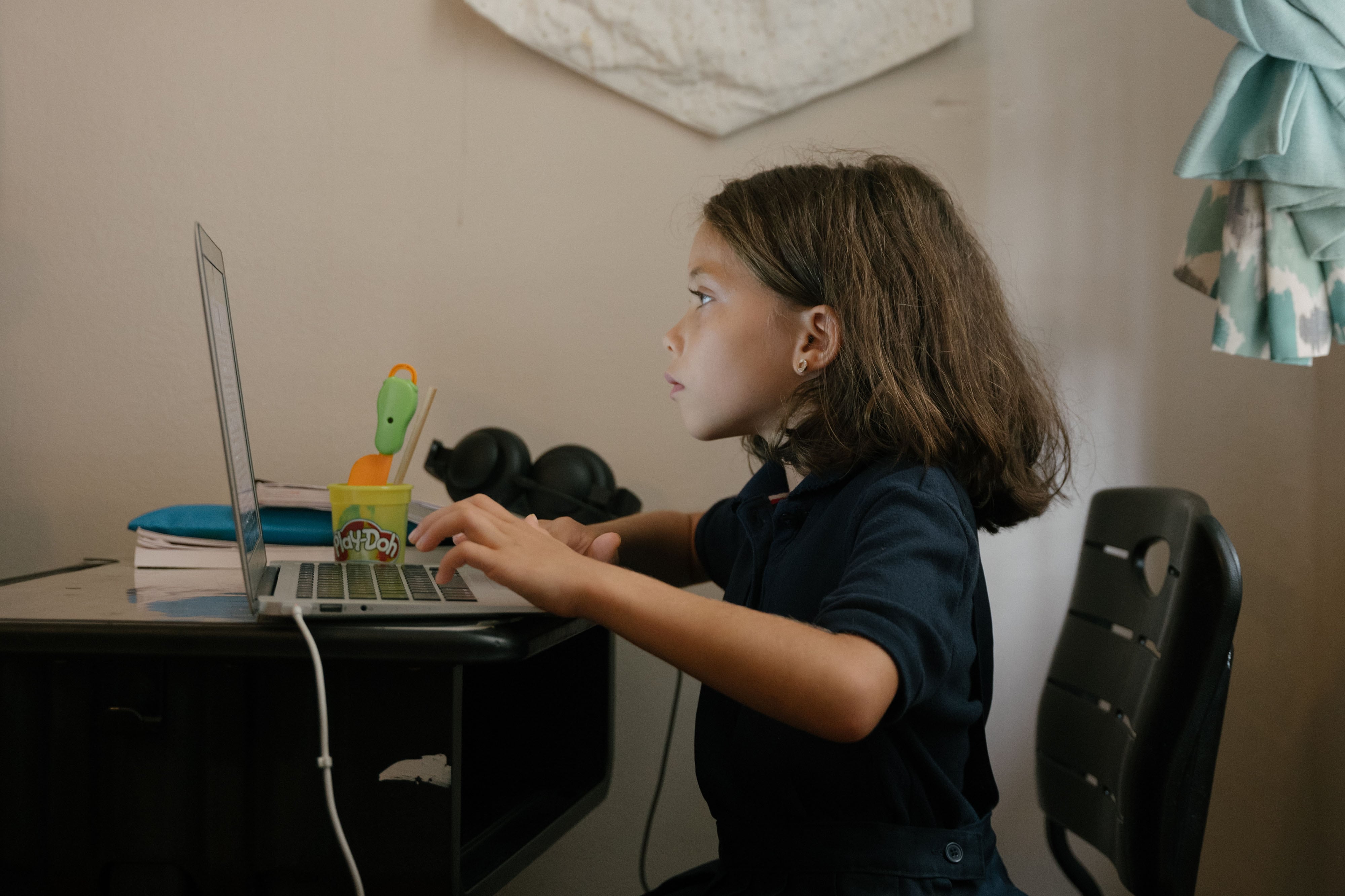 A young girl is sitting at a desk and working on a computer.