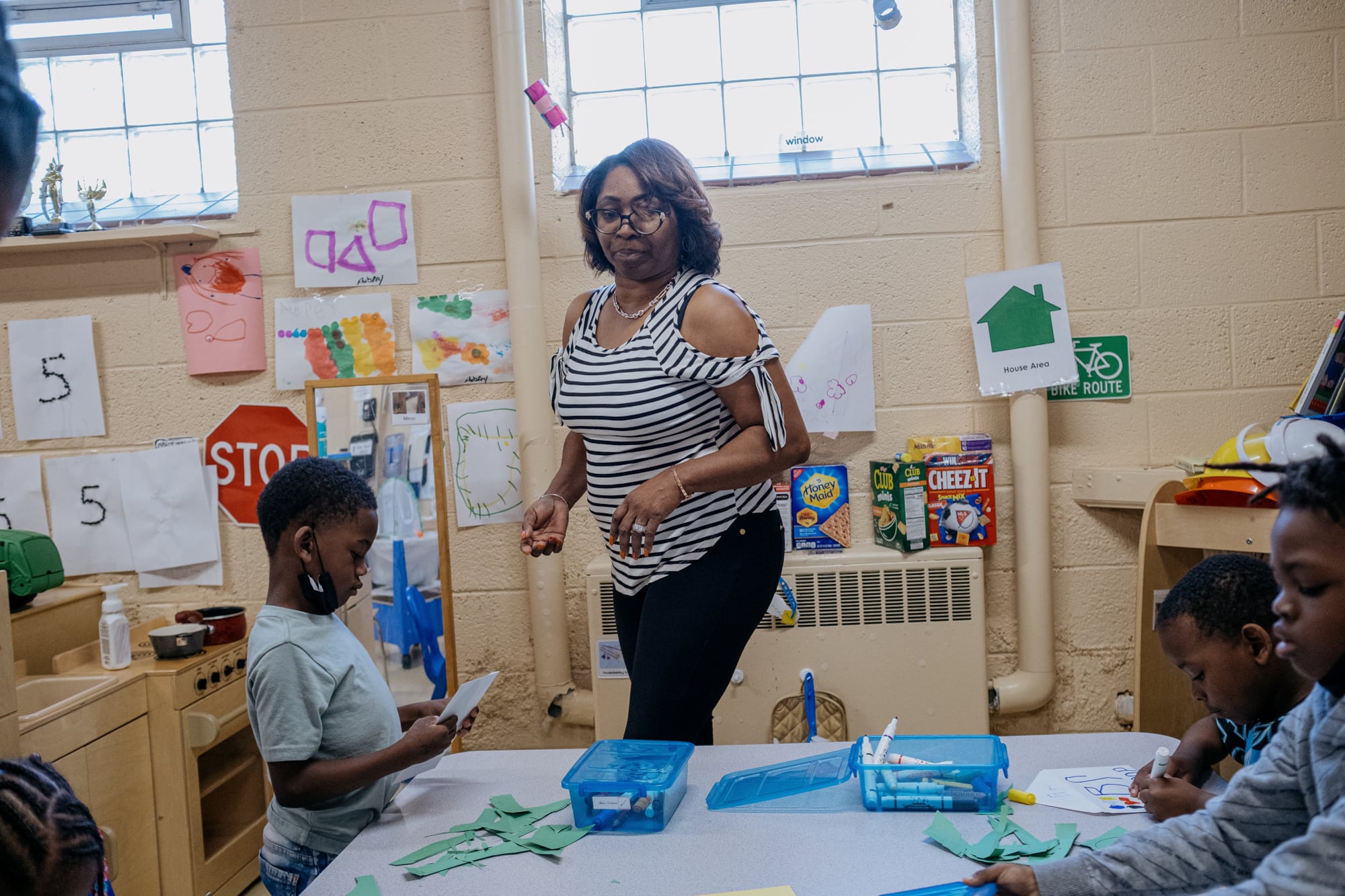 An adult walks by a table full of young students in classroom.