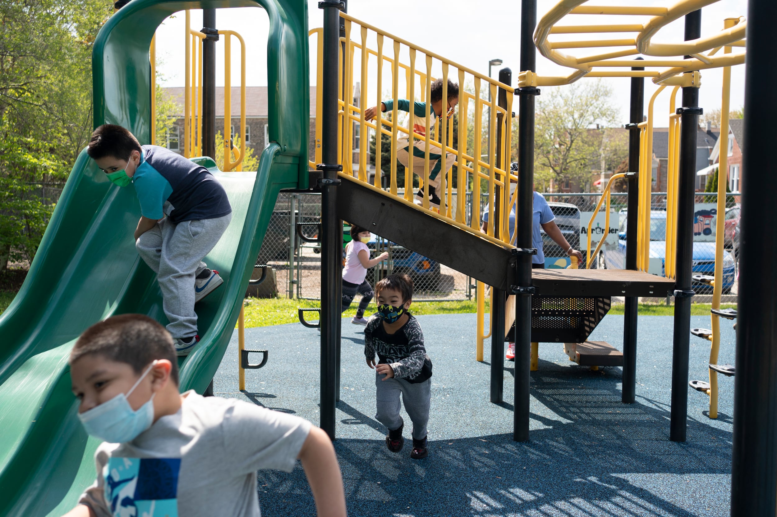 Several children play on a green and yellow outdoor play structure in Chicago.