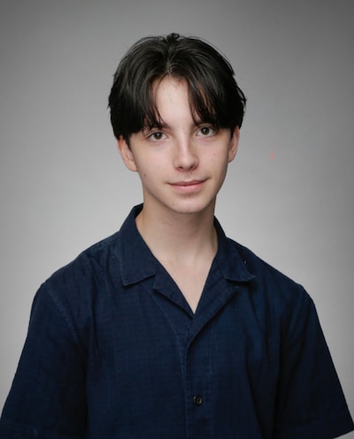 A photograph of a high school student with short dark hair and wearing a blue shirt posing for a photograph against a tan background.
