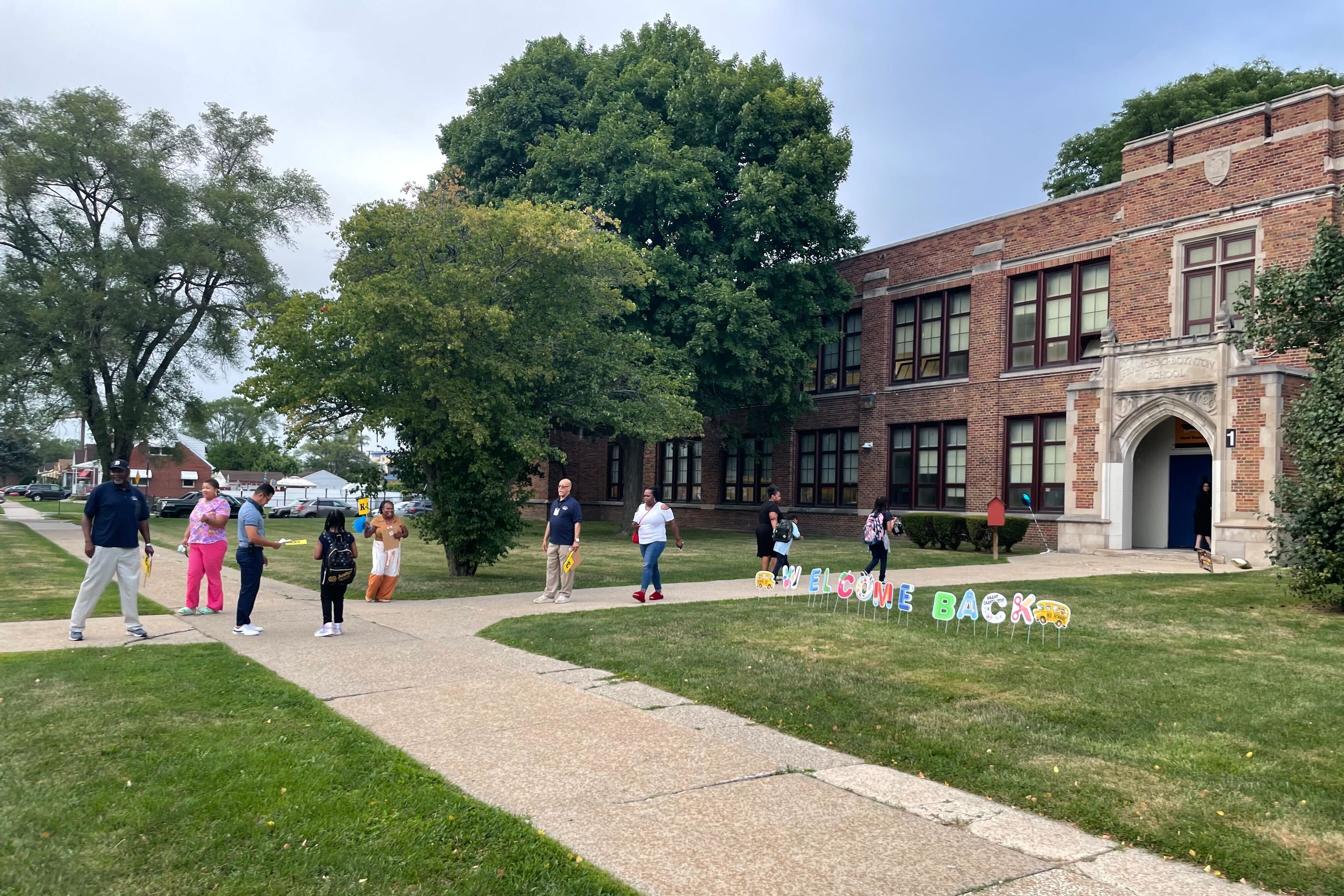 A school building is shown as parents walk their children to school on the first day in the Detroit school district. A welcome back sign is displayed in the lawn.