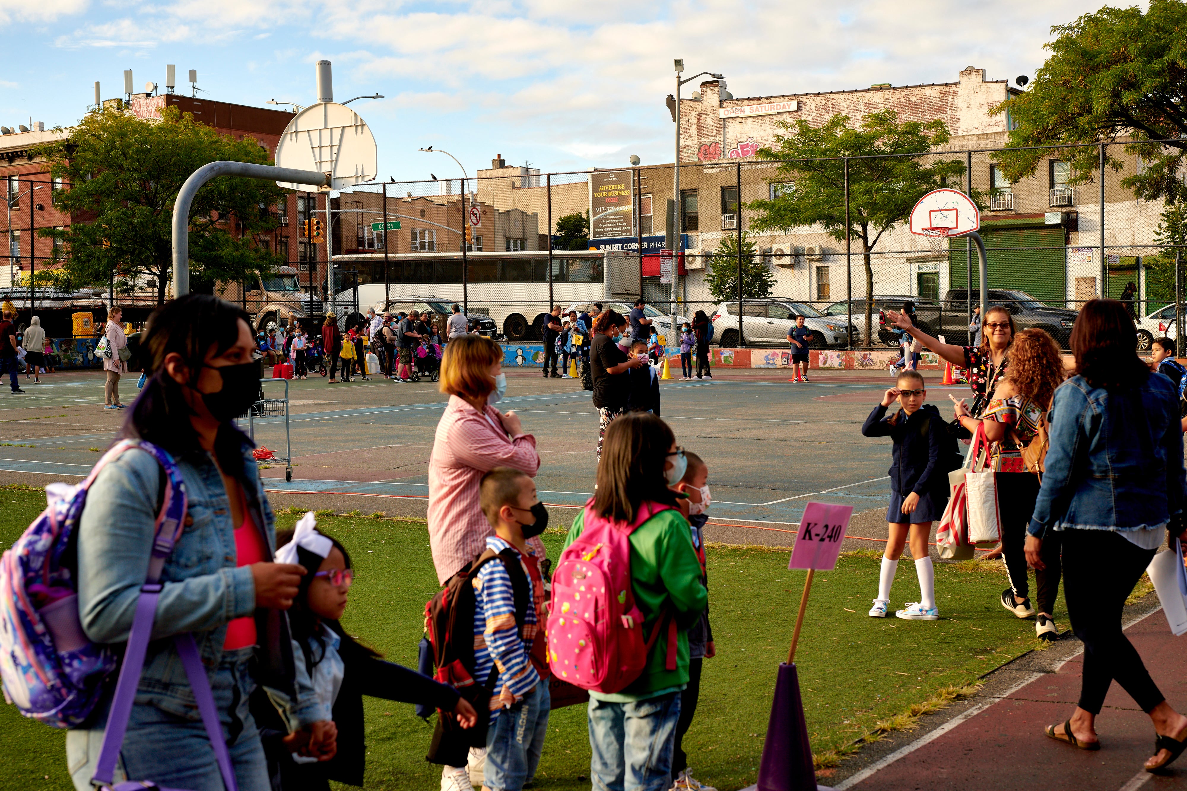 Parents and children walk outside of a school, with basketball courts visible in the background.