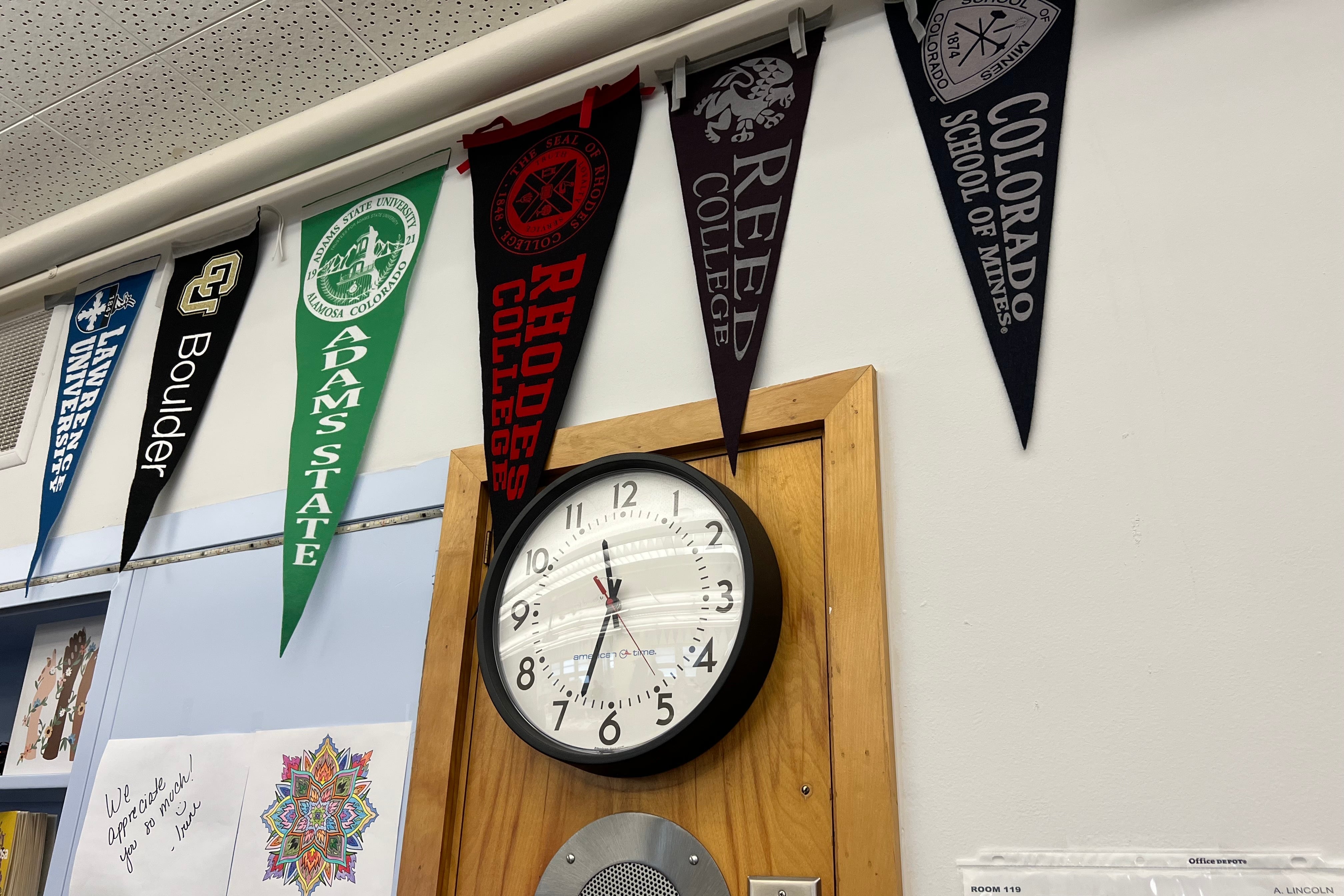 College pennant flags hang inside Lincoln High School in Denver above a clock.