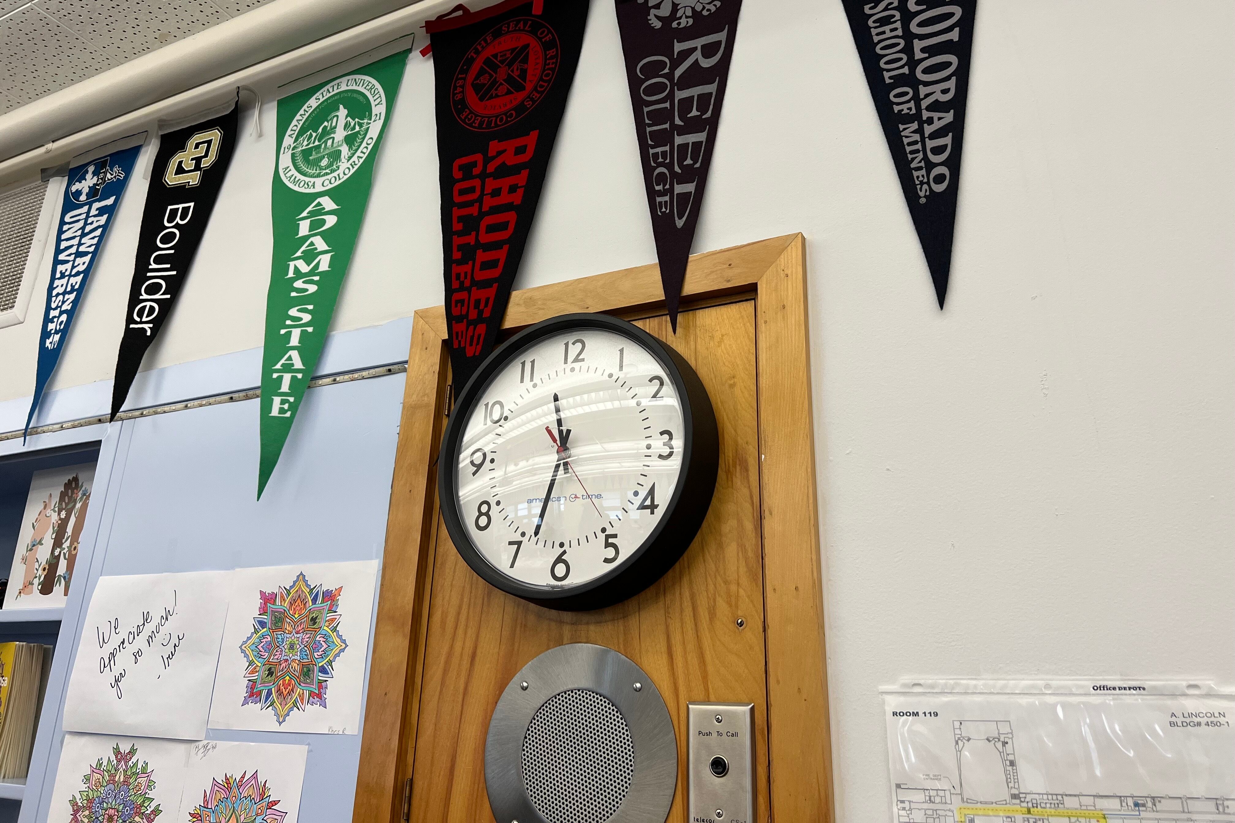 College pennant flags hang inside Lincoln High School in Denver above a clock.
