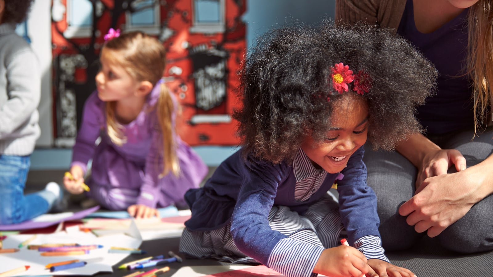 A photo of two preschool-age girls coloring on the floor.