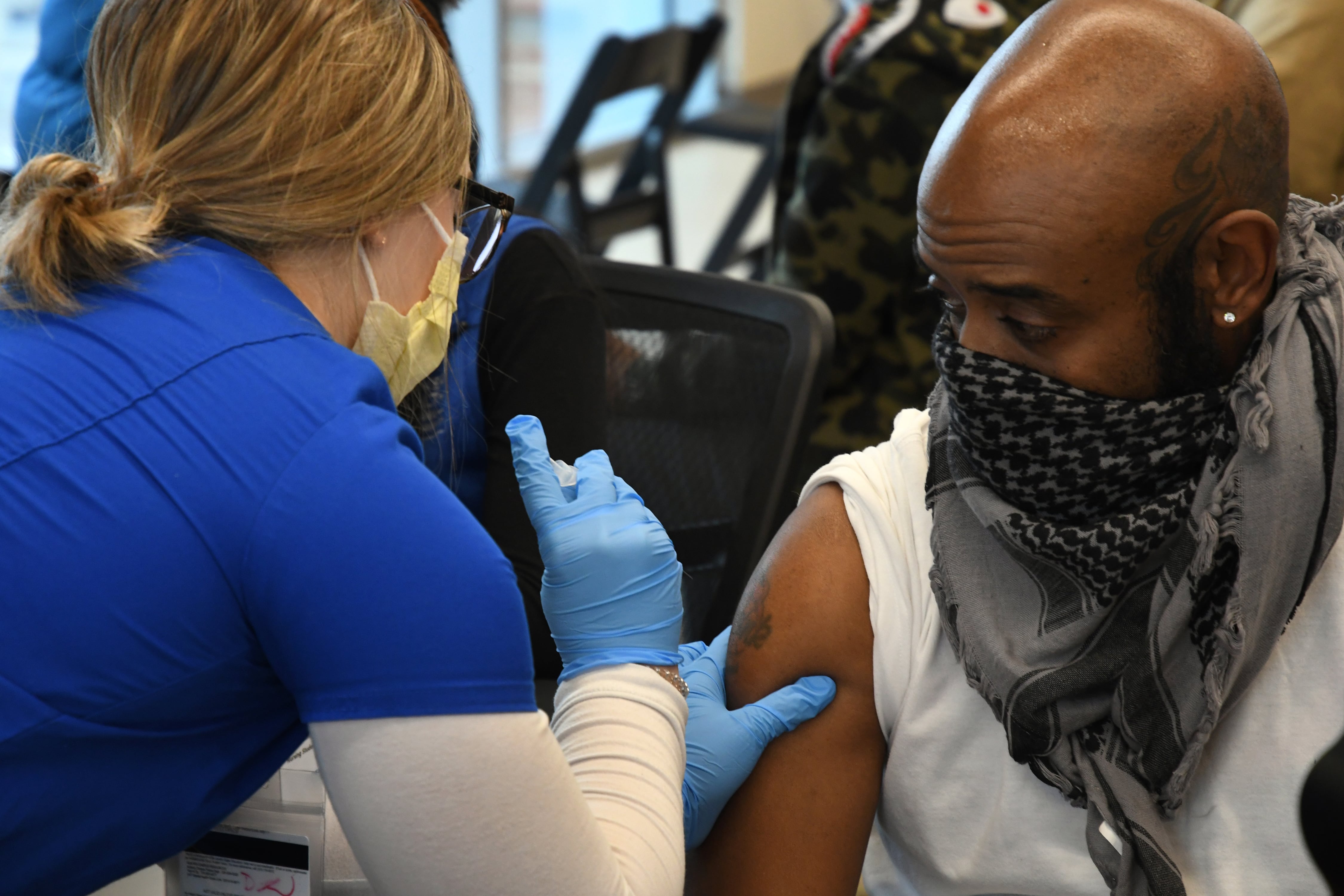 A woman wearing gloves and a mask gives a vaccine to a man wearing a mask.