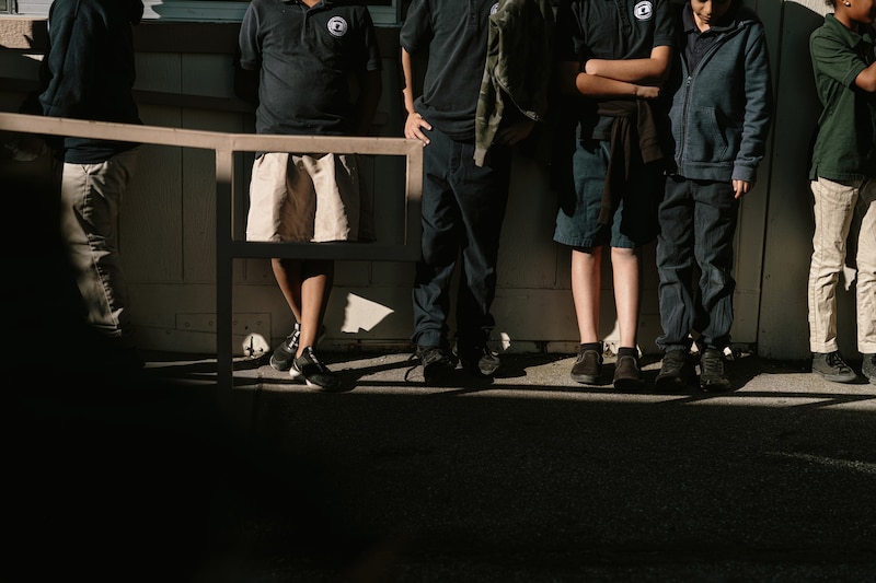 A photograph of a line of students standing against a wall. No view of their faces.