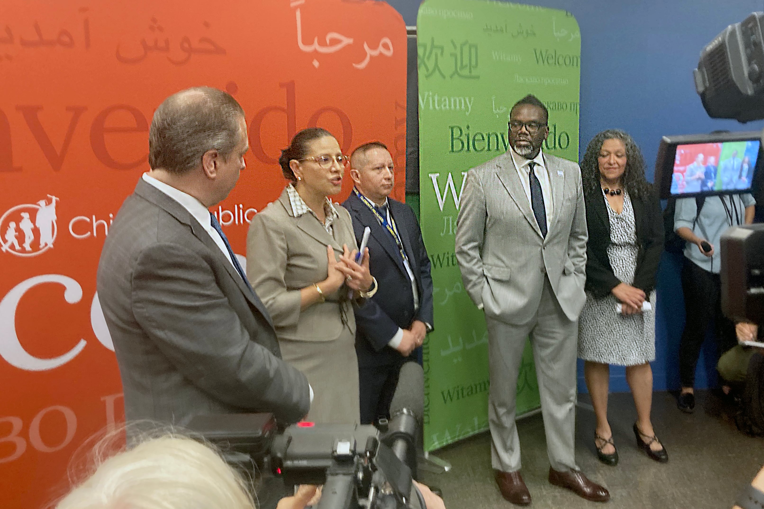 Chicago Public Schools CEO Pedro Martinez and Mayor Brandon Johnson stand in front of an orange and green sign outside a new enrollment center for newcomer families to get children enrolled before the first day of school.