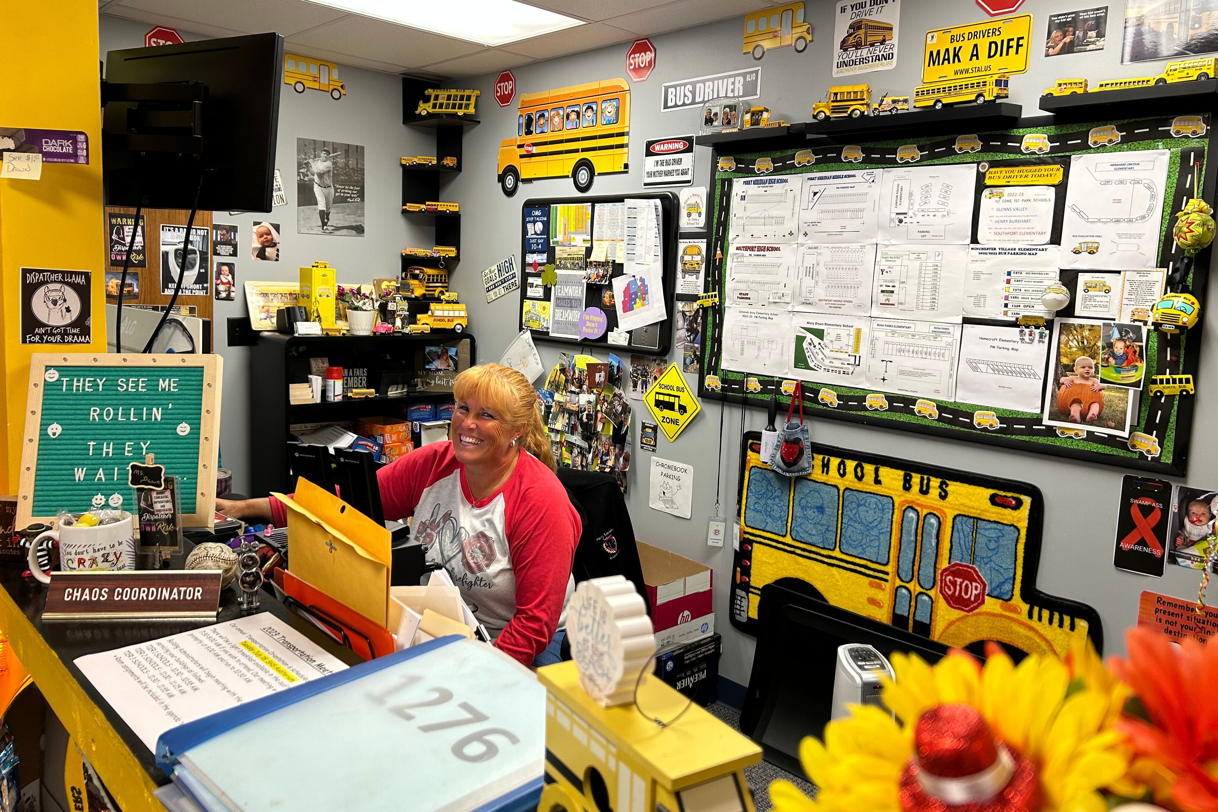 A woman in a white shirt with red sleeves smiles in a room decorated with yellow school buses.