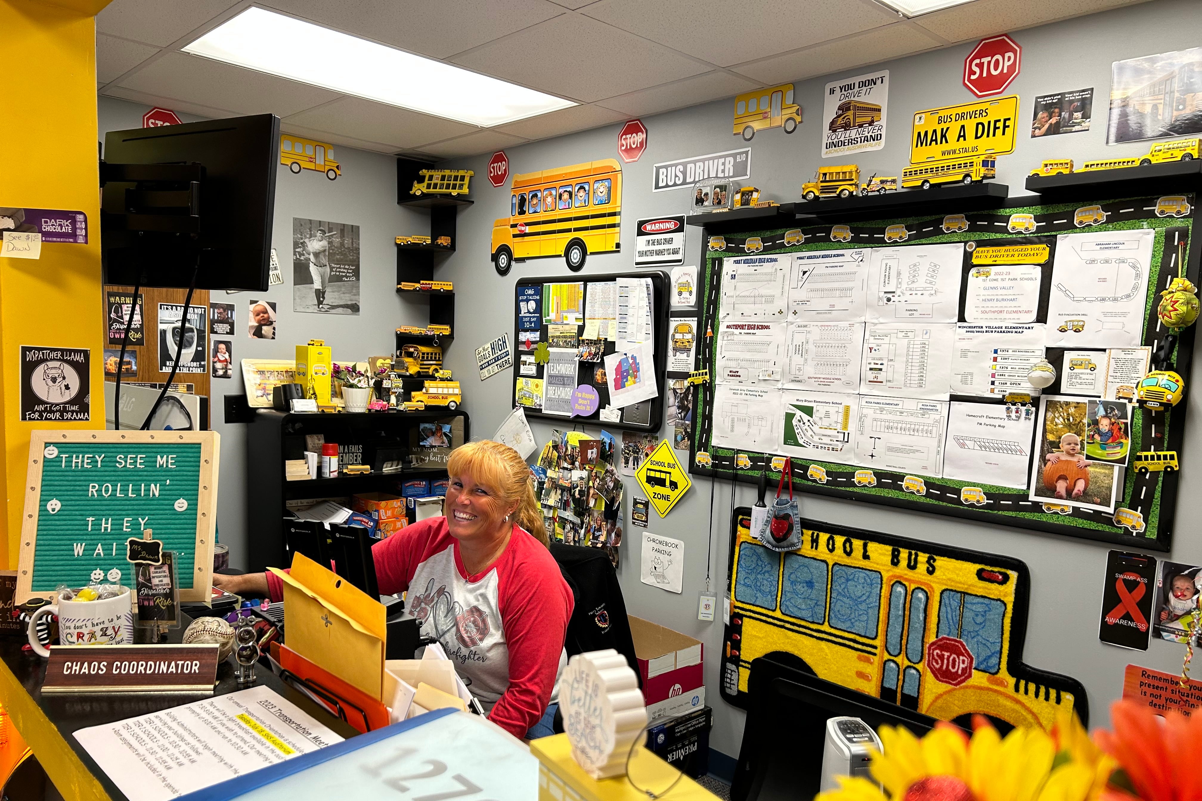 A woman in a white shirt with red sleeves smiles in a room decorated with yellow school buses.