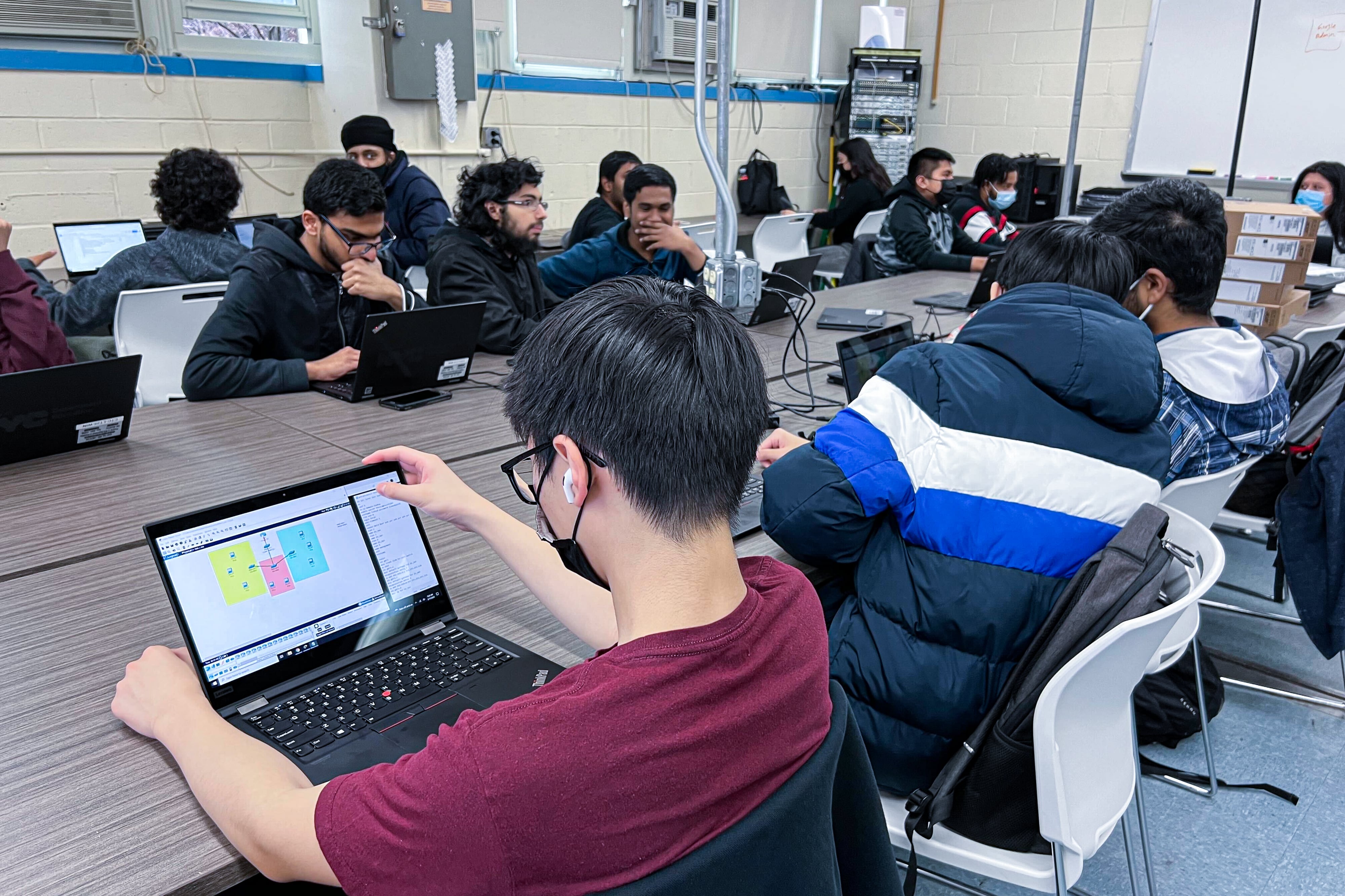 Students sitting at a table at school working on computers.