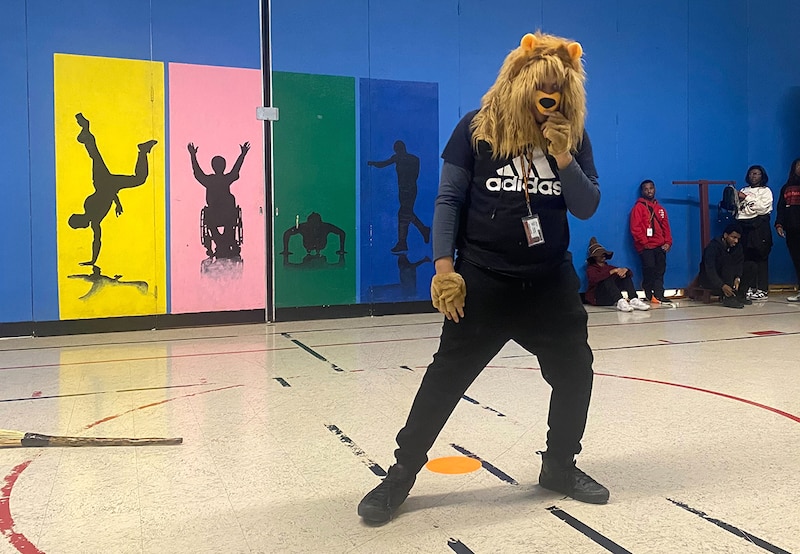 A student in a black outfiot and a lion head stands in a gym.