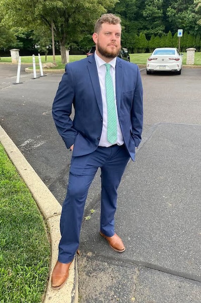 A man in a blue suit and green tie stands in a parking lot.