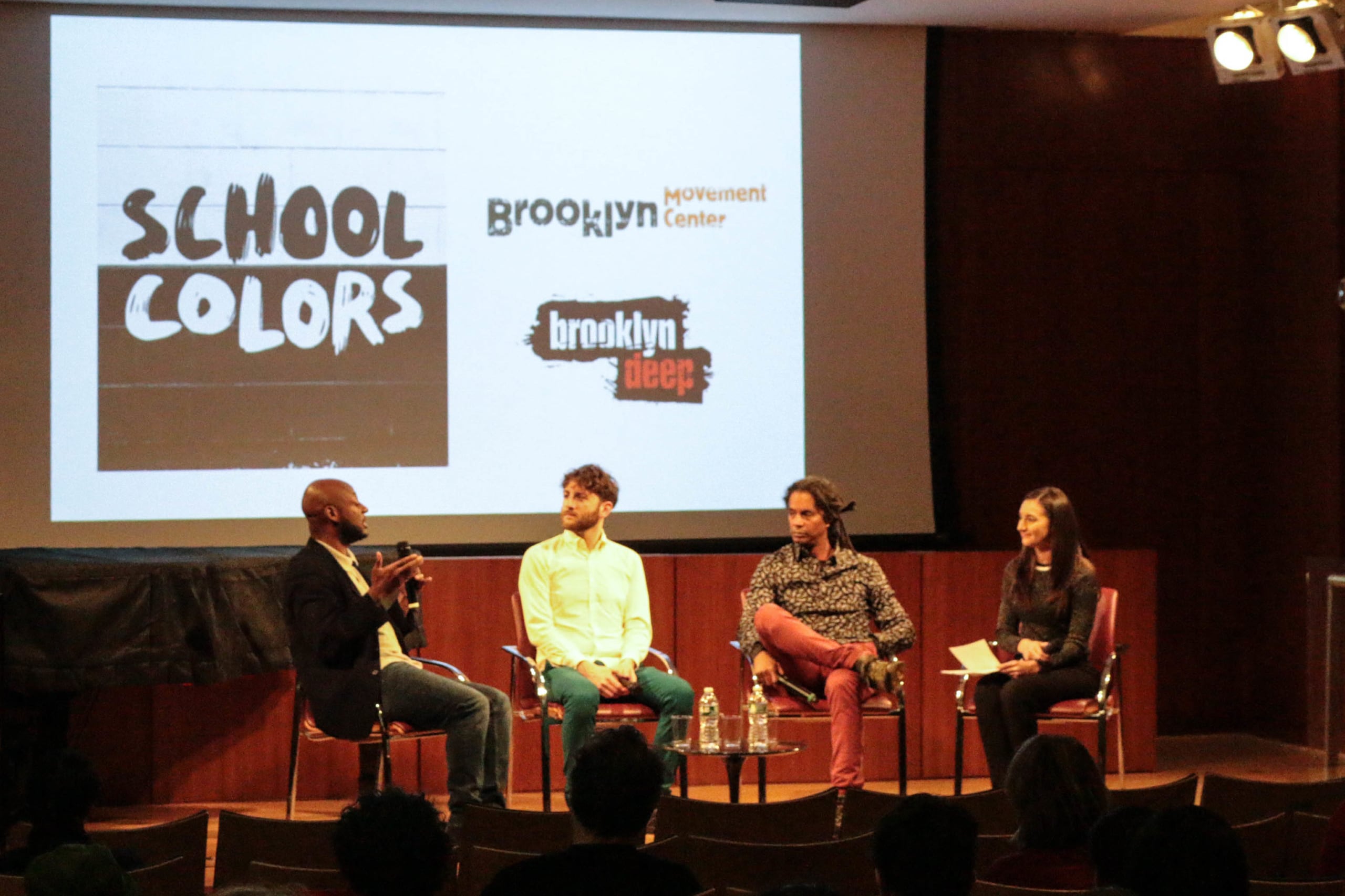 Four people sit in chairs on a stage in front of a projected image
