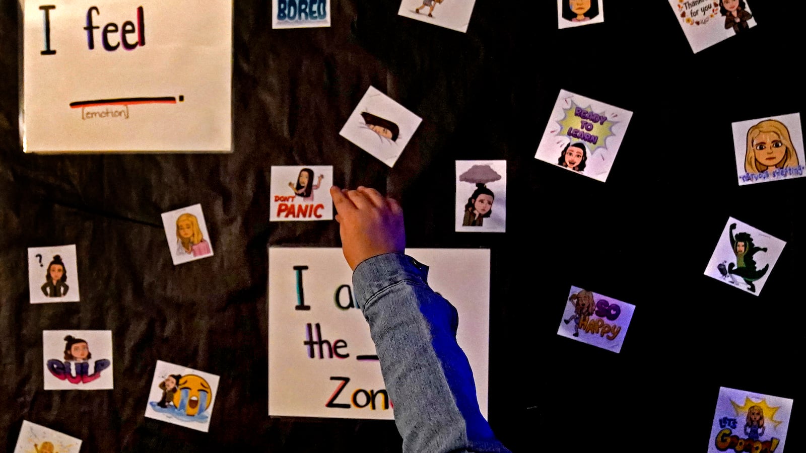 An elementary school student points to markers indicating her feelings on a black wall.