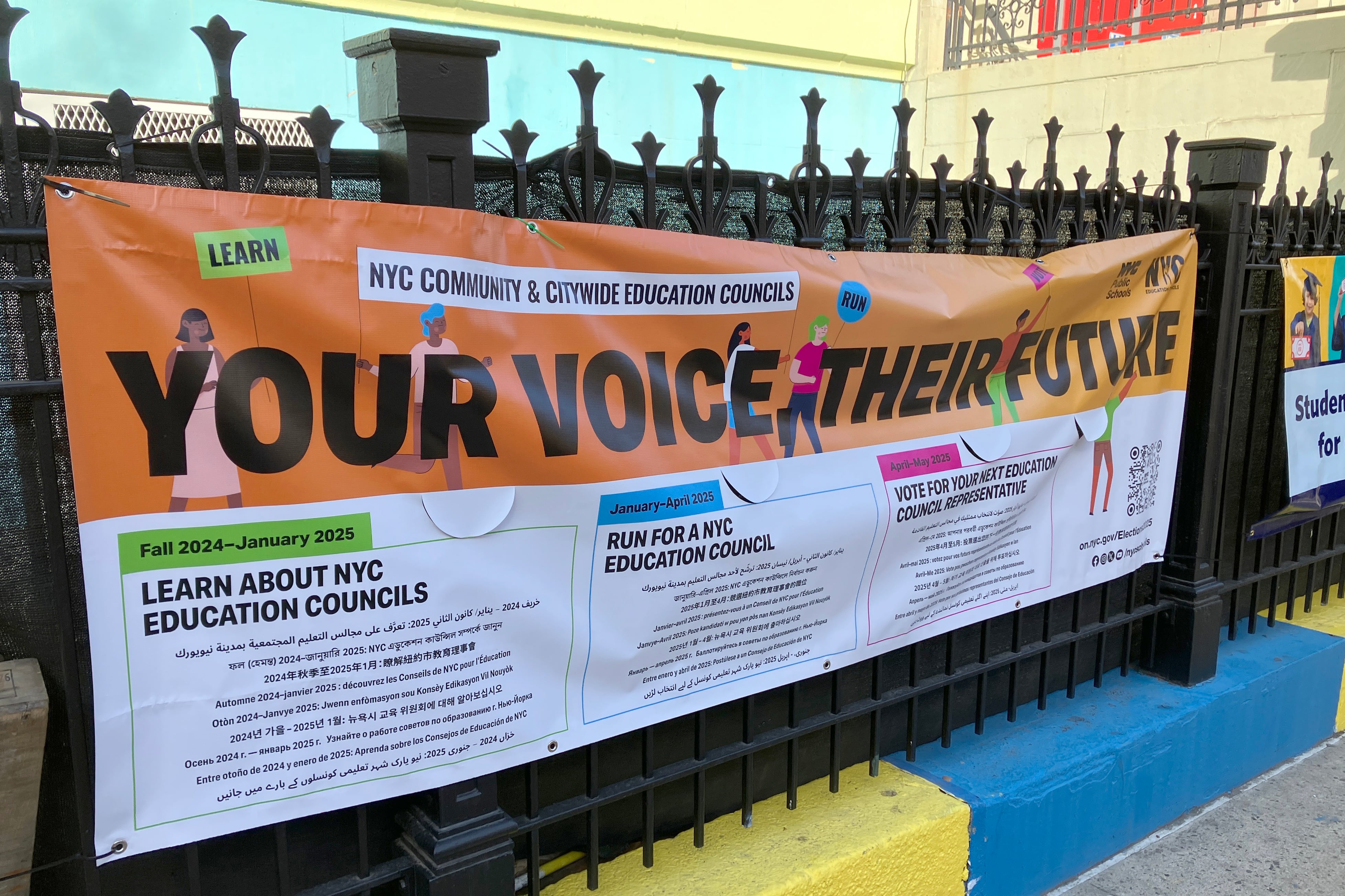 A colorful sign hanging on a black metal fence.