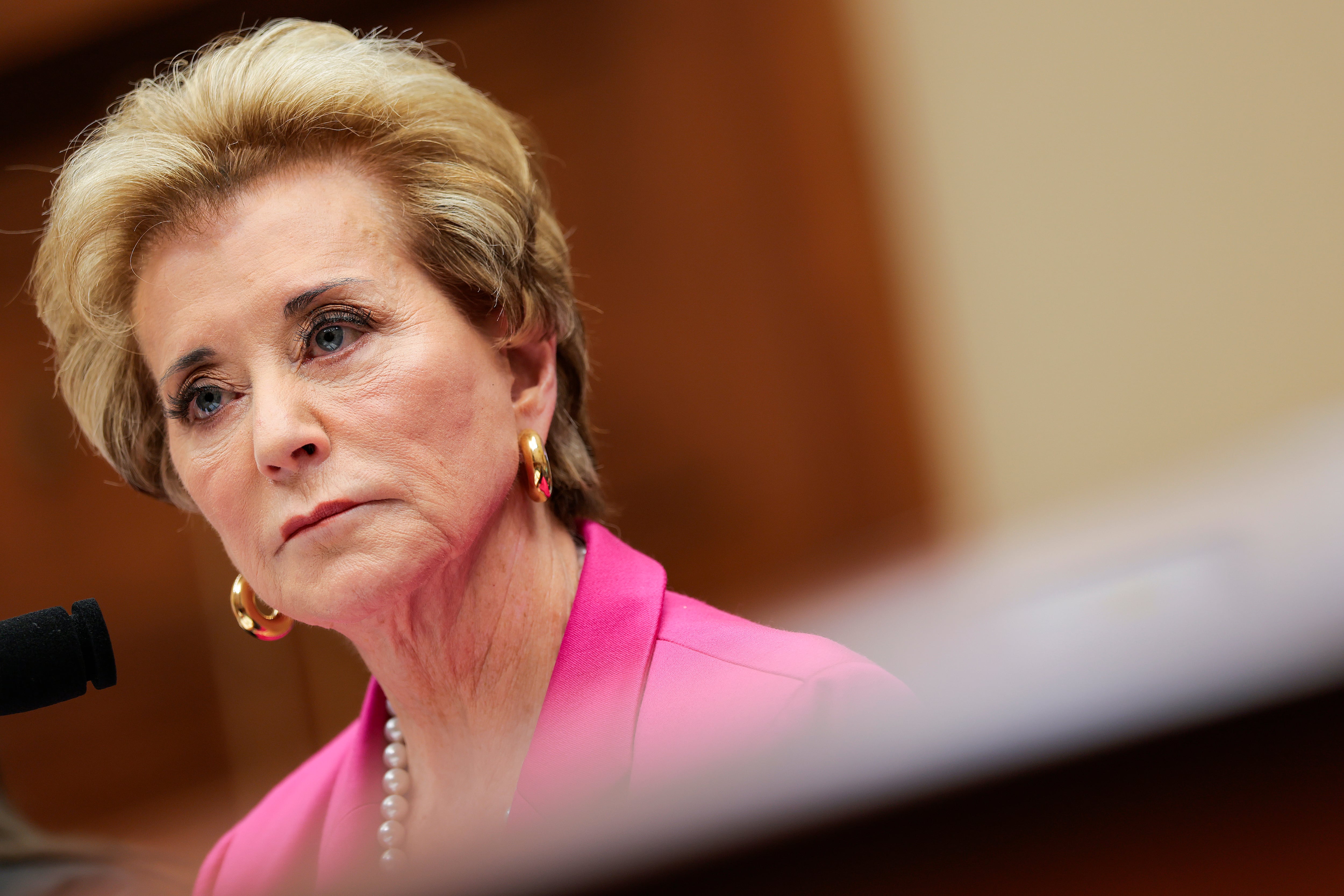 A woman in a pink suit jacket and earrings listens.