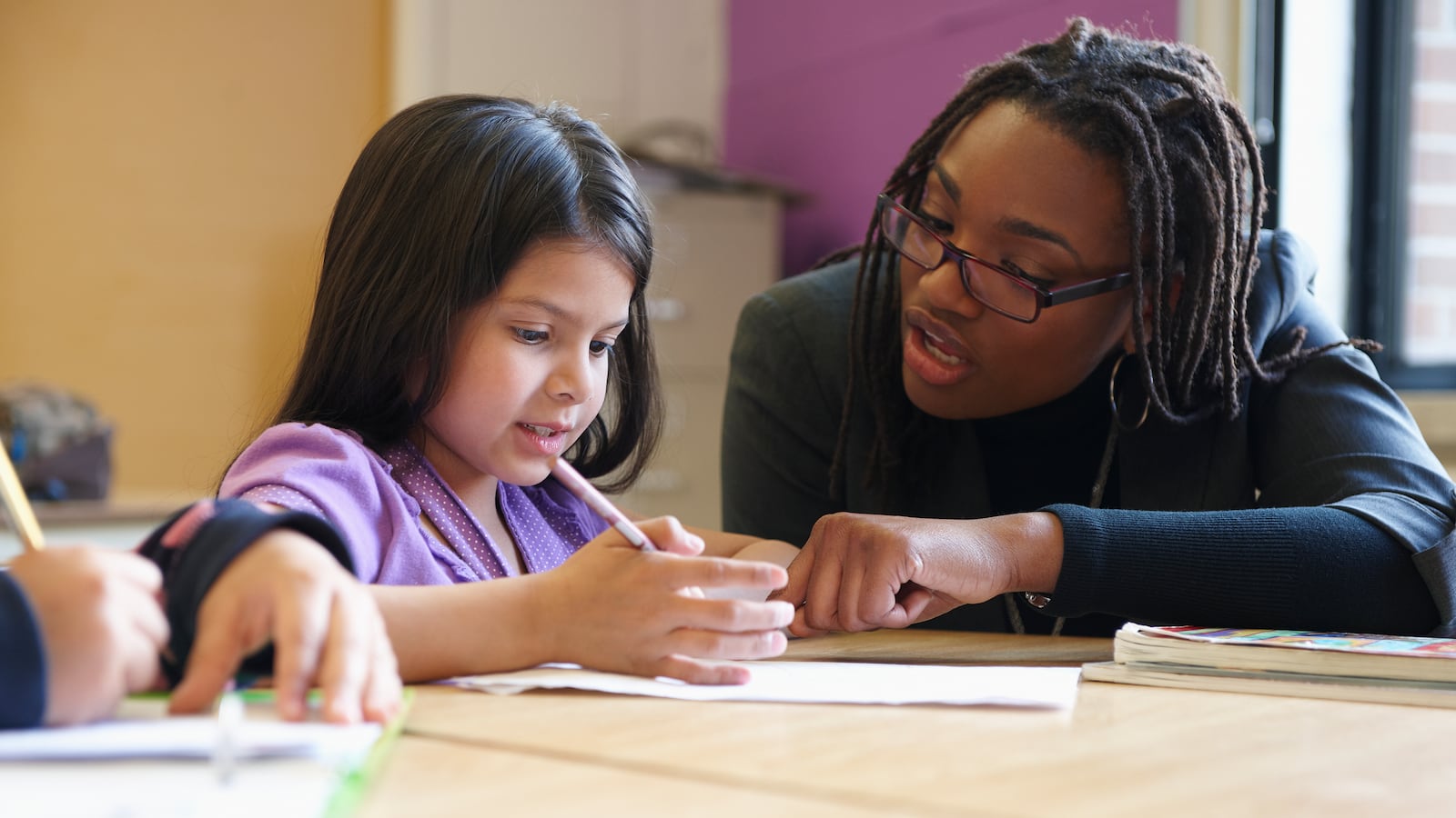 A teacher assists an elementary school student at a desk.