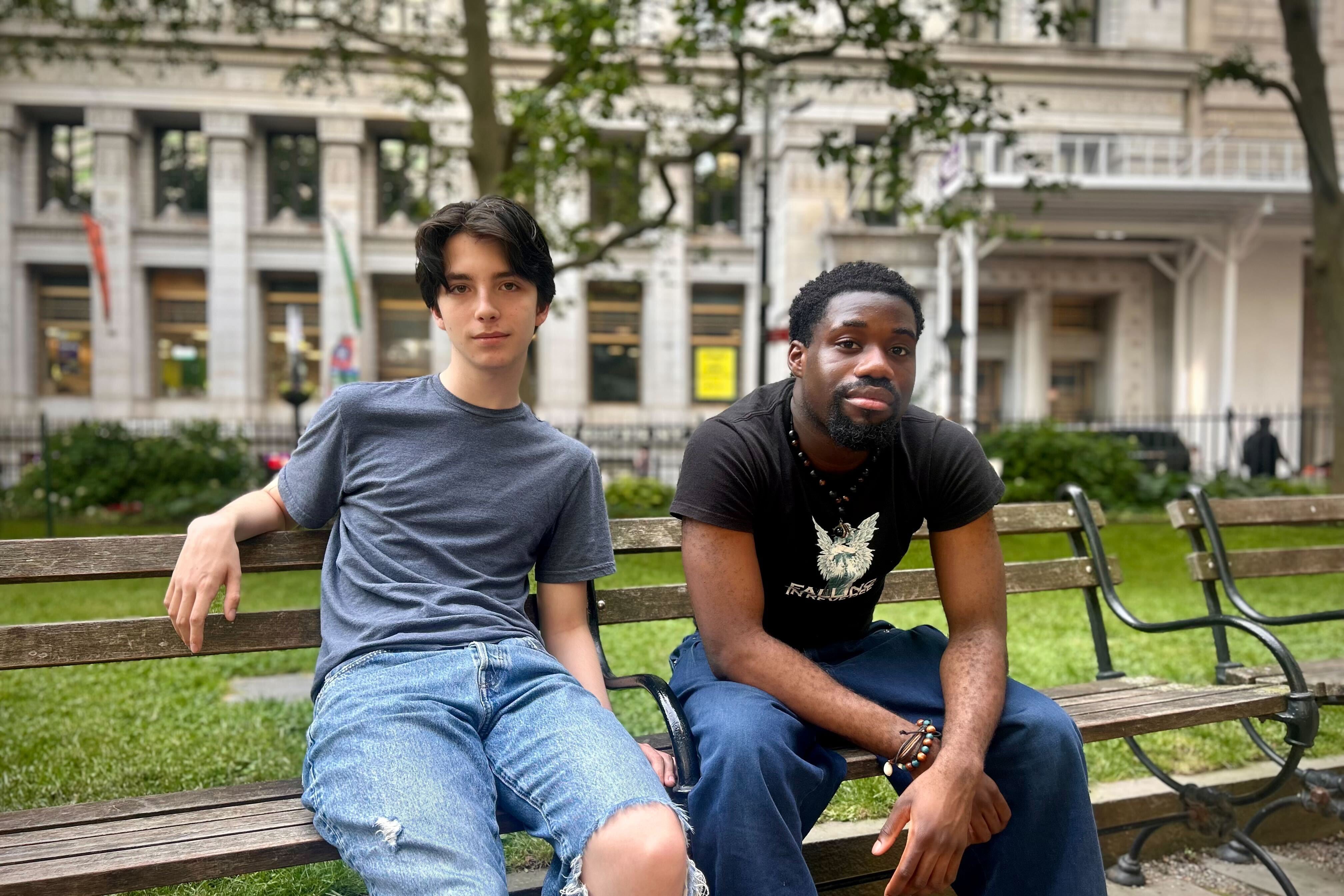 Two high school students sit next to each other on a park bench posing for a photograph.