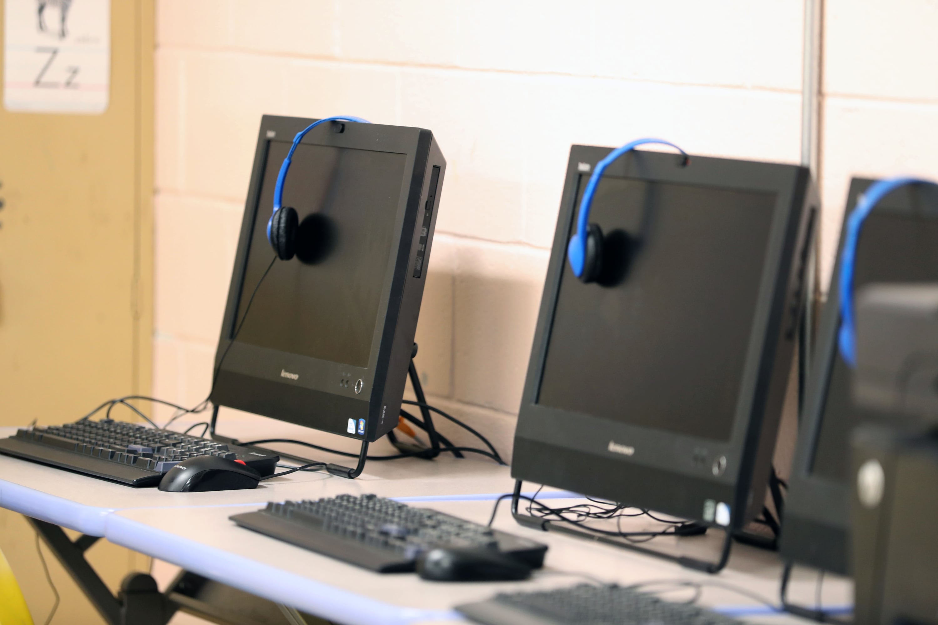 A photograph of three school computers on a desk.
