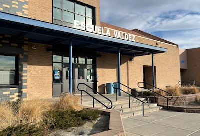 The front entrance of a tan brick school building with words that read "Escuela Valdez" above a set of steps in the front.