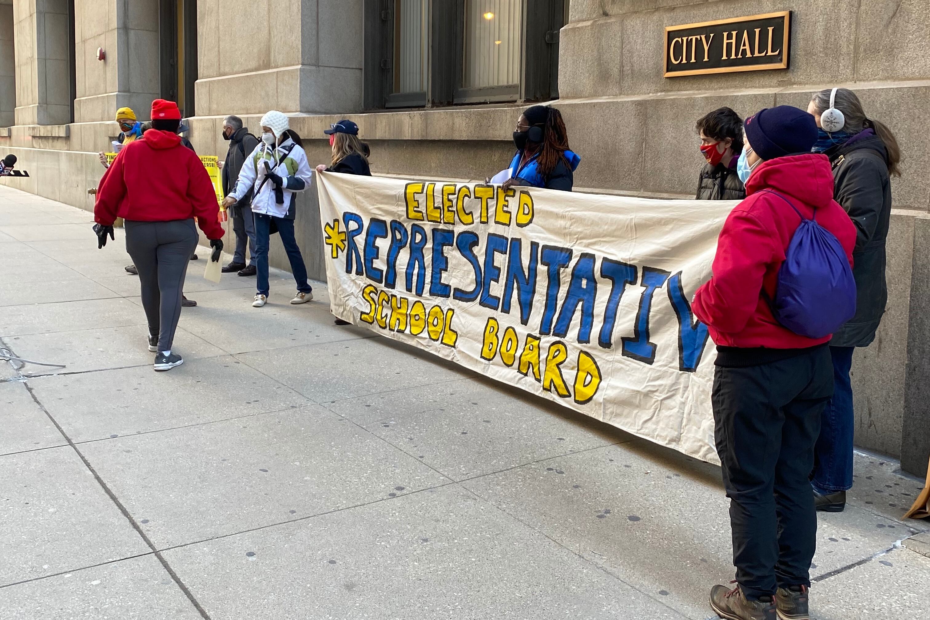 Advocates for an elected school board hold a banner outside of City Hall.