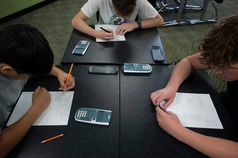 Three students work at tables.