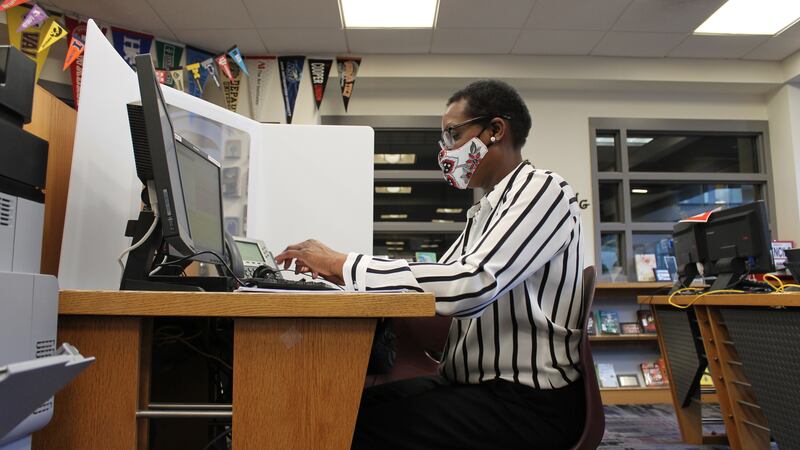 Woman in a striped shirt and wearing a mask sits at a desk working on a laptopl