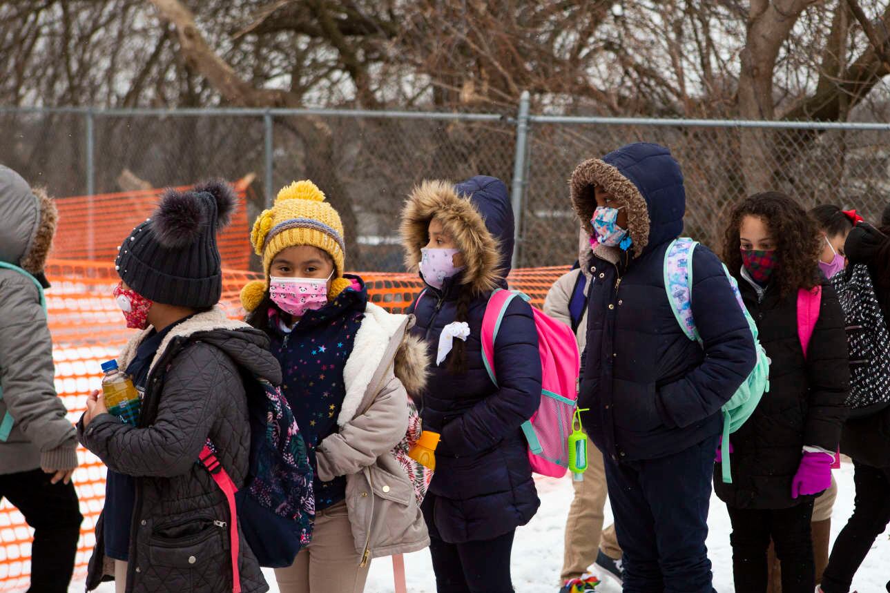 Masked students wait in line to enter a Grand Rapids school building
