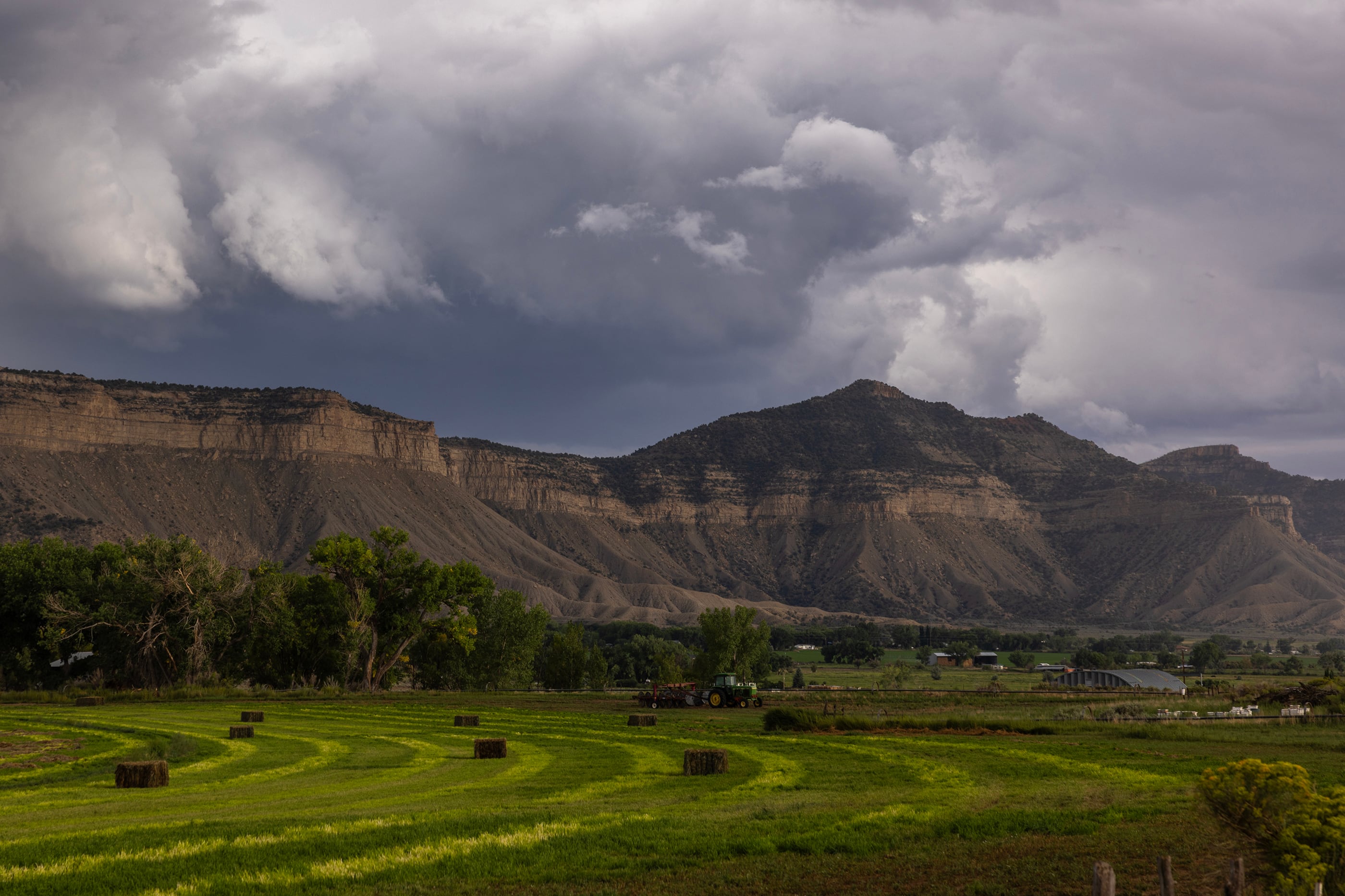 Farmland with bails of hay in a valley with a mountain and some houses in the background.