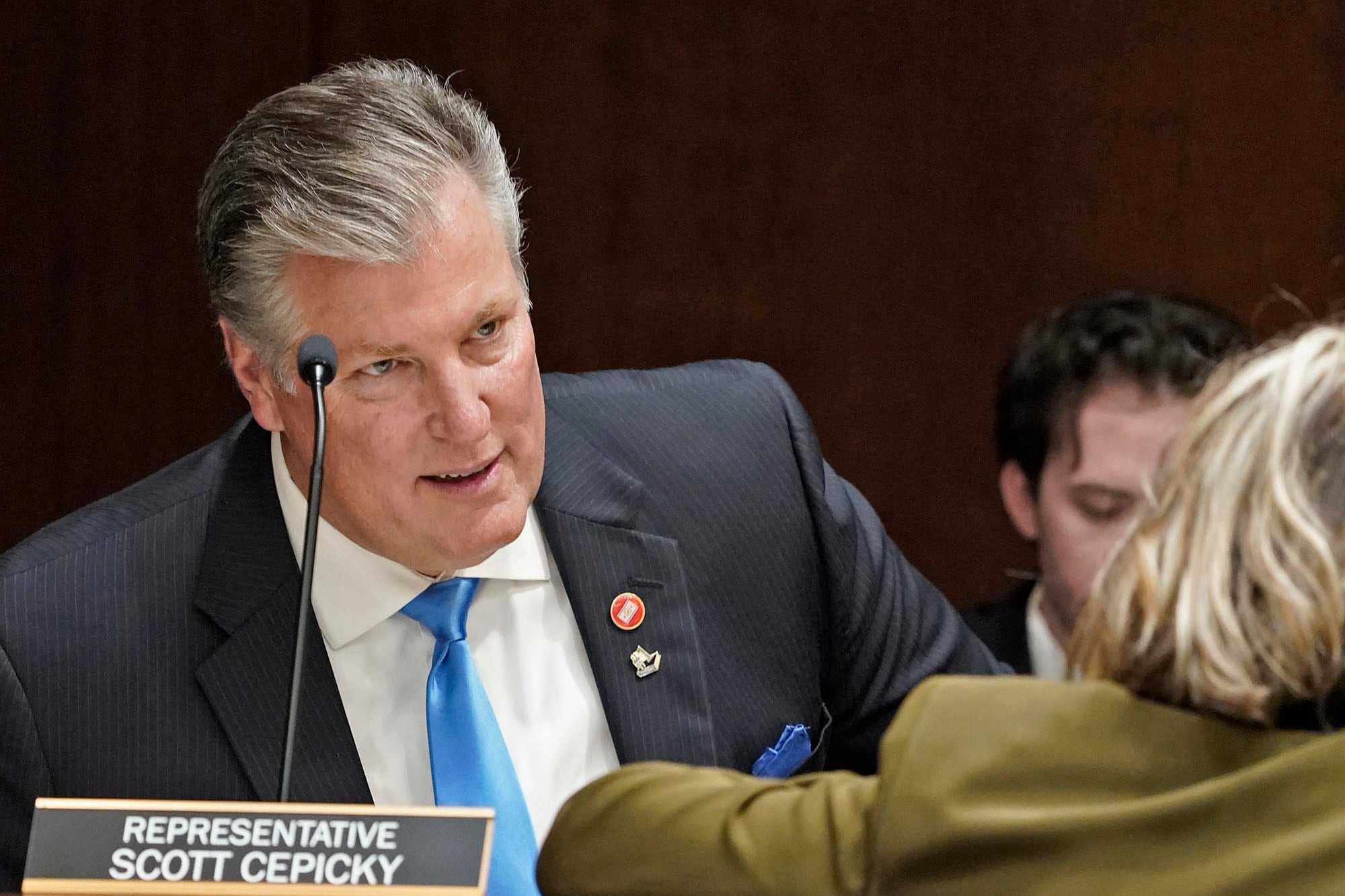 A man wearing a business suit leans over a desk to speak with a woman.