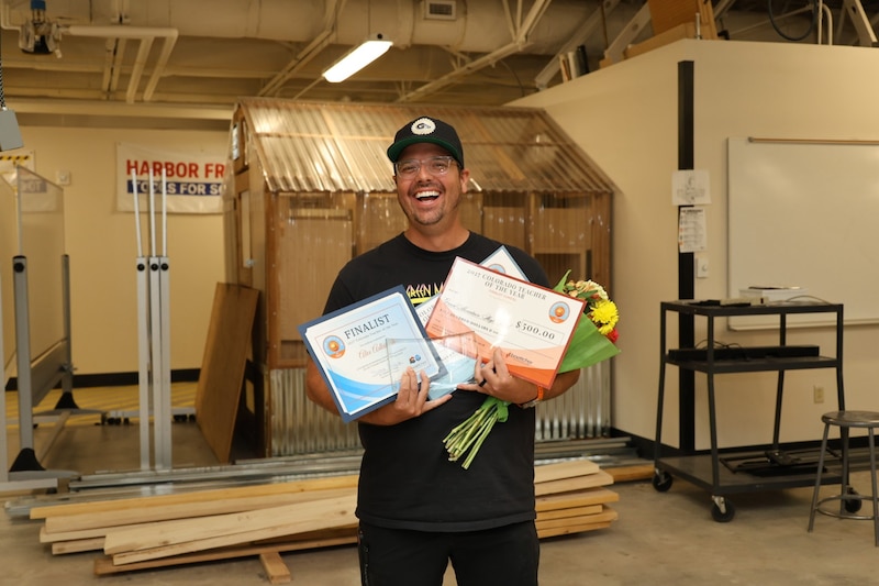 A man wearing a dark ballcap holds certificates and flowers.