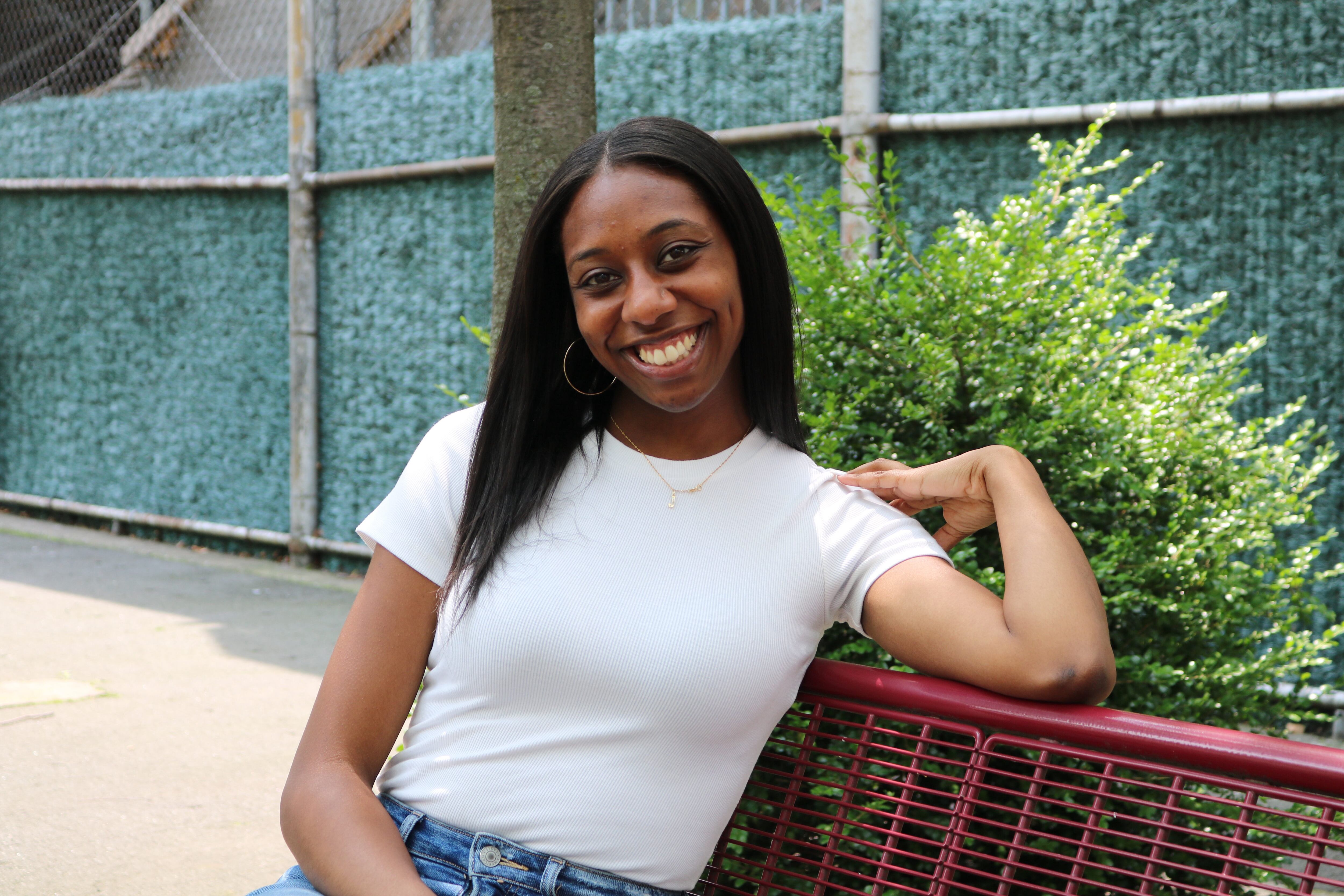 A photograph of a Black woman with medium-length black hair sitting on a bench, smiling.