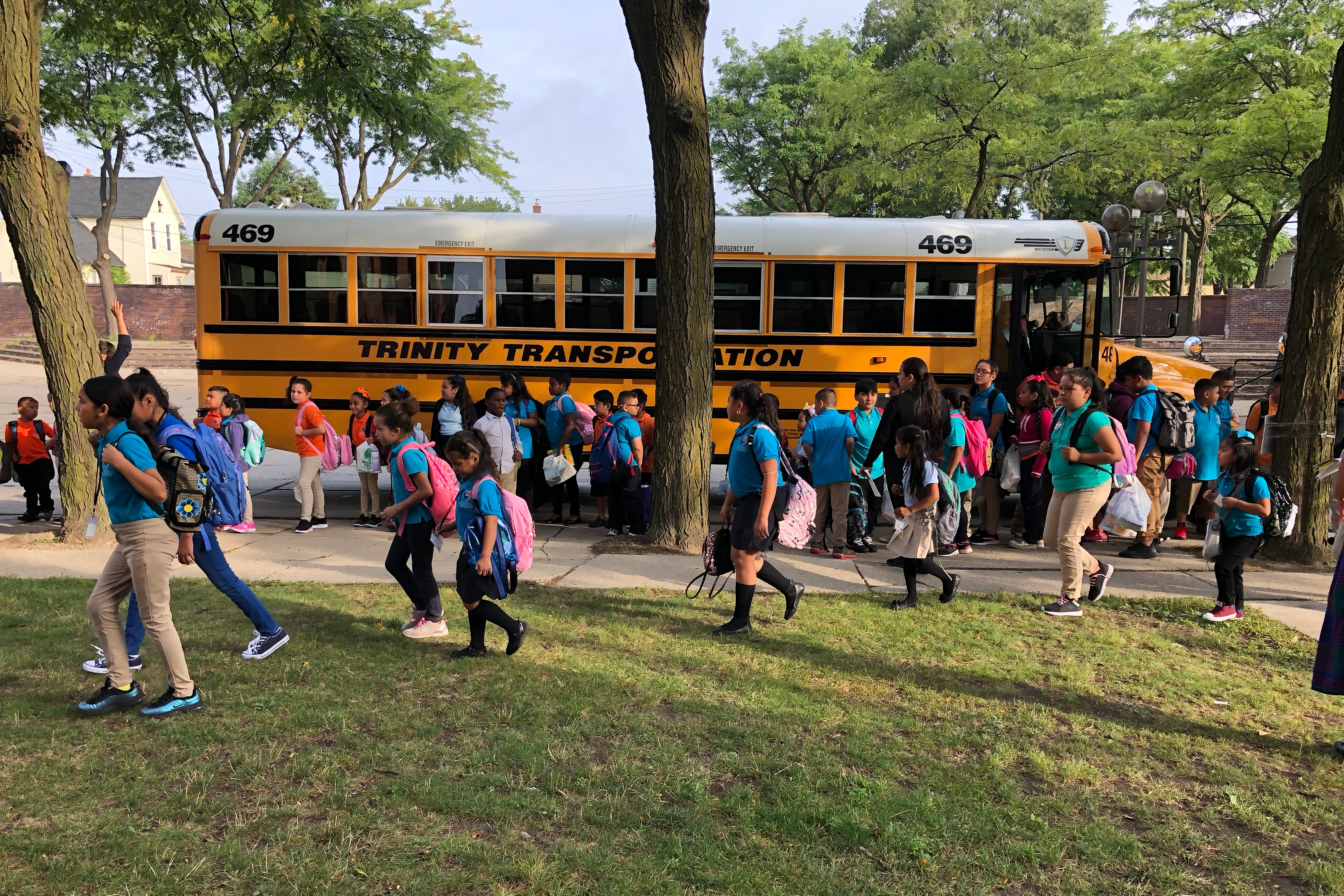 Students walk in a large crowd in front of yellow school buses.