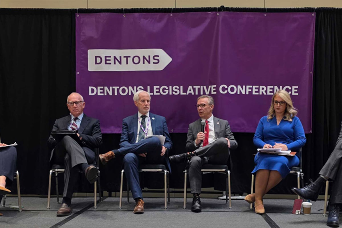 A line of six people sits in front of a purple sign.