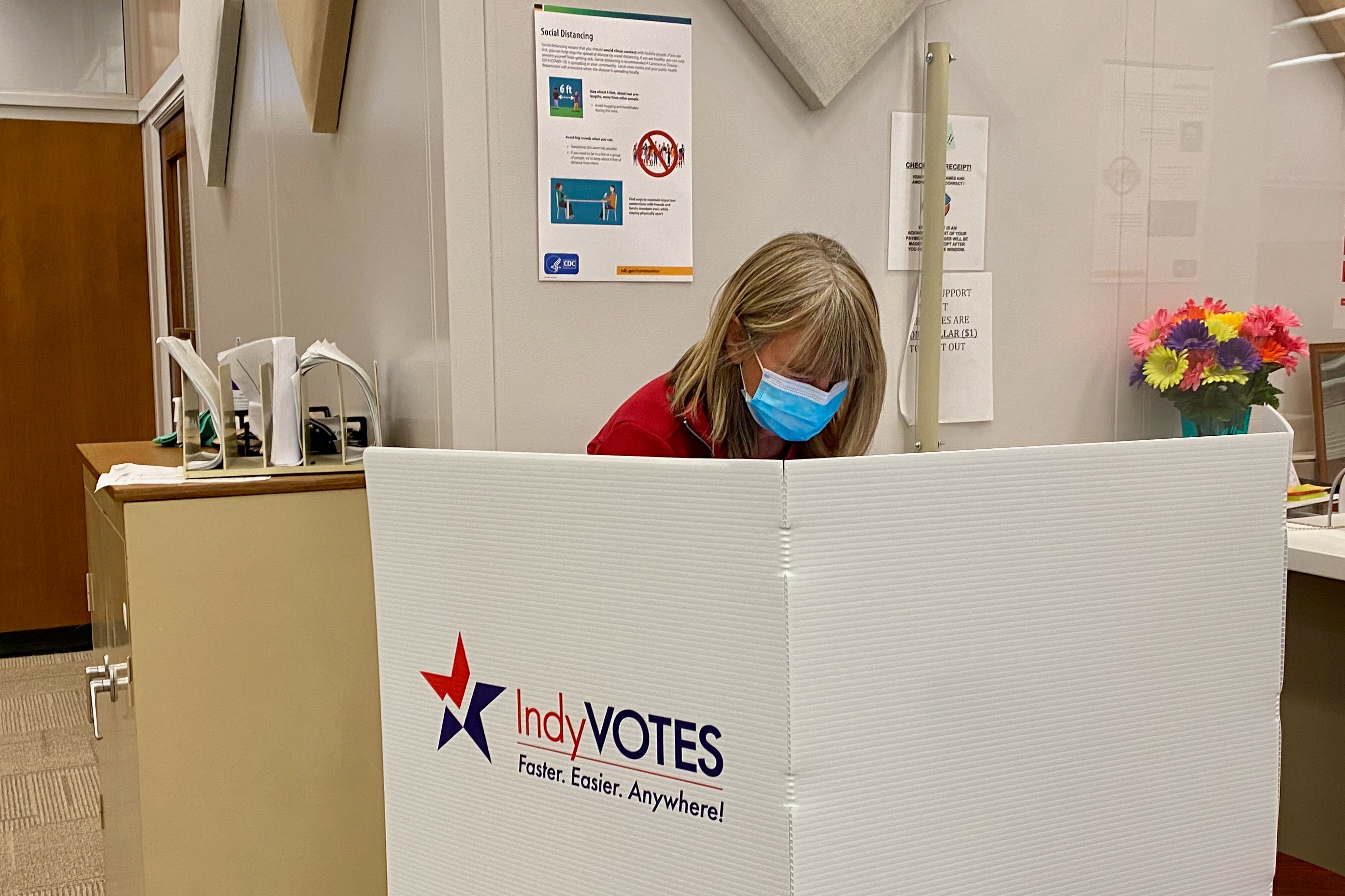 A woman stands behind a voting screen that says IndyVOTES
