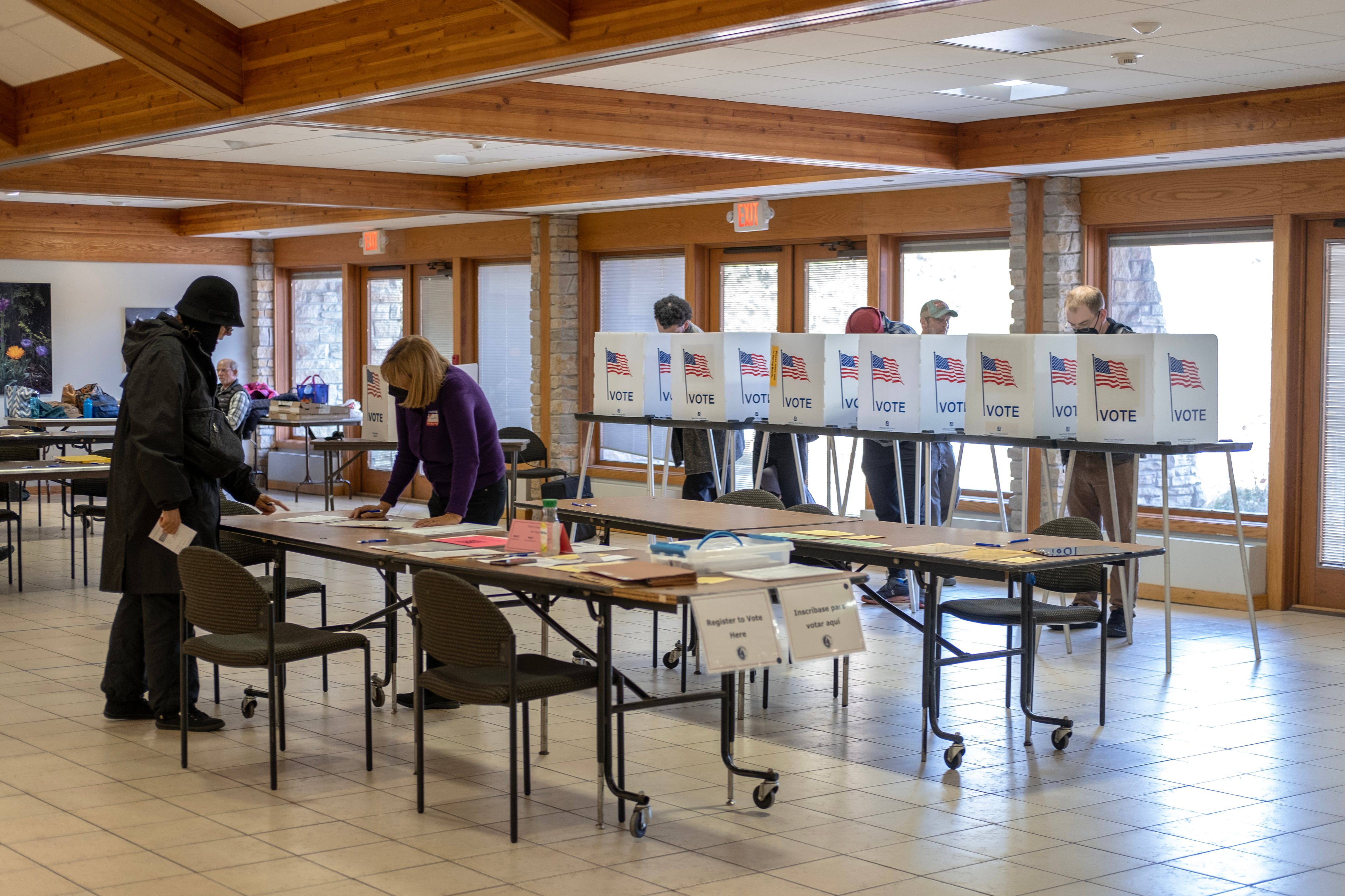 Two people talk over a table while four people vote in the background.