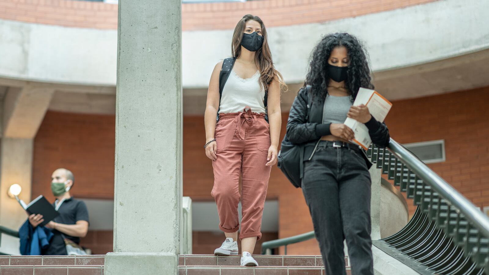 A group of college students wearing protective face masks walk down steps inside a university building.