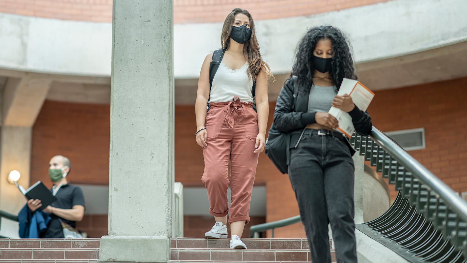 A group of college students wearing protective face masks walk down steps inside a university building.