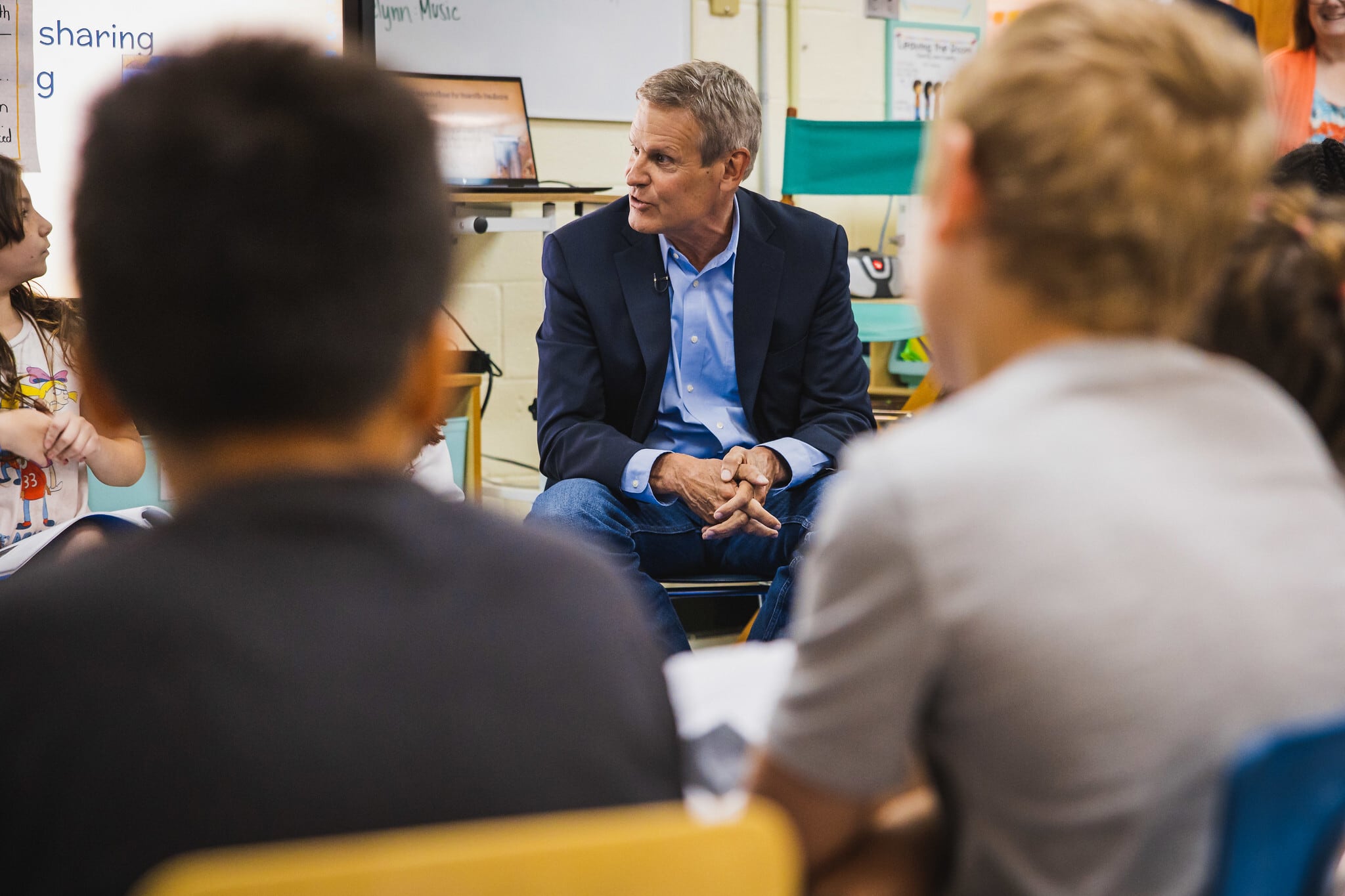 A man in a blue suit sits between two people in a classroom.